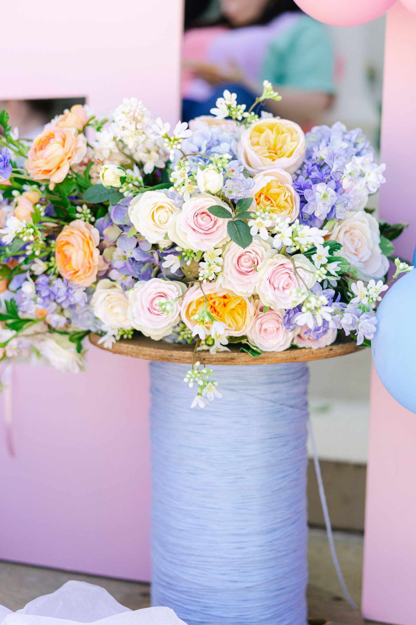 Colorful pastel floral arrangement sitting atop a light blue spool-styled pedestal.