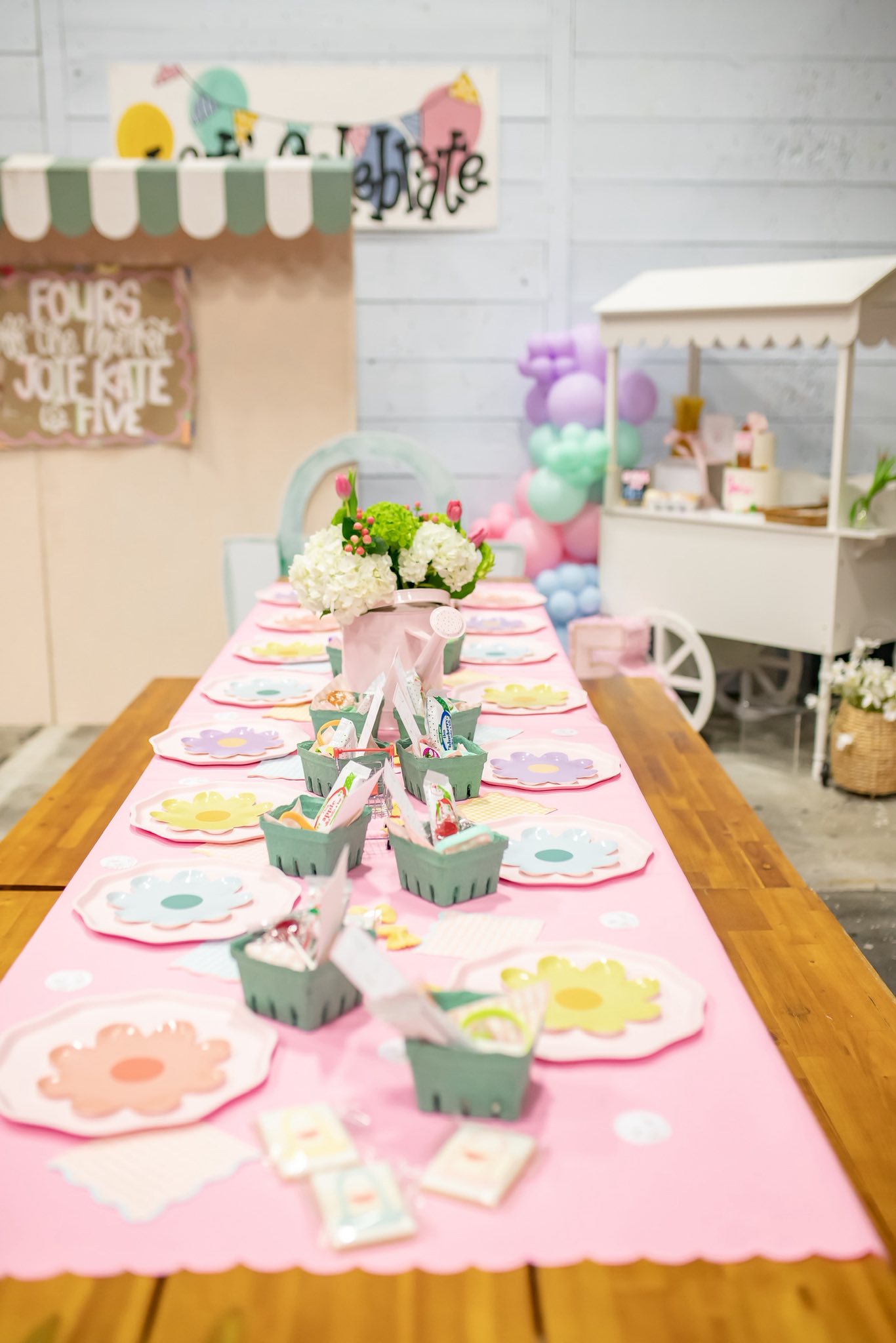 Table set for a party with pink tablecloth, flower-shaped plates, and small green berry baskets.