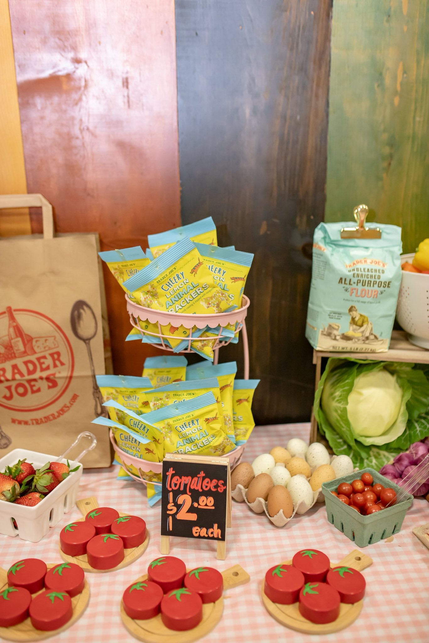 Display of Trader Joe's Cheery Lemon Animal Crackers on a counter with produce, eggs, flour, and toy wooden tomatoes.