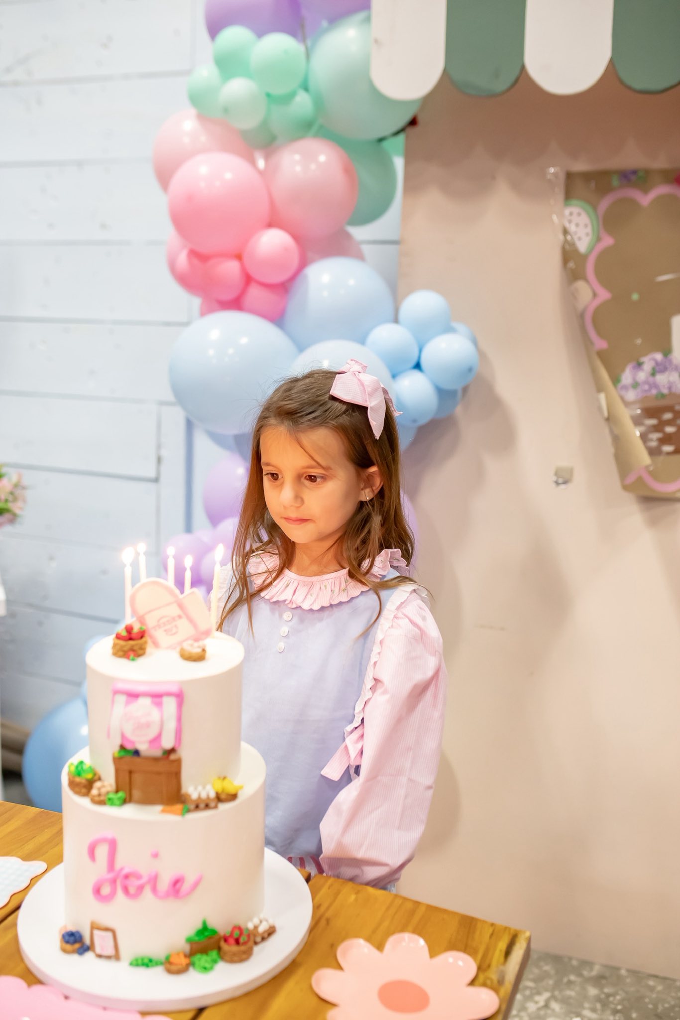 Young girl in a light blue and pink dress standing in front of a two-tiered birthday cake with candles