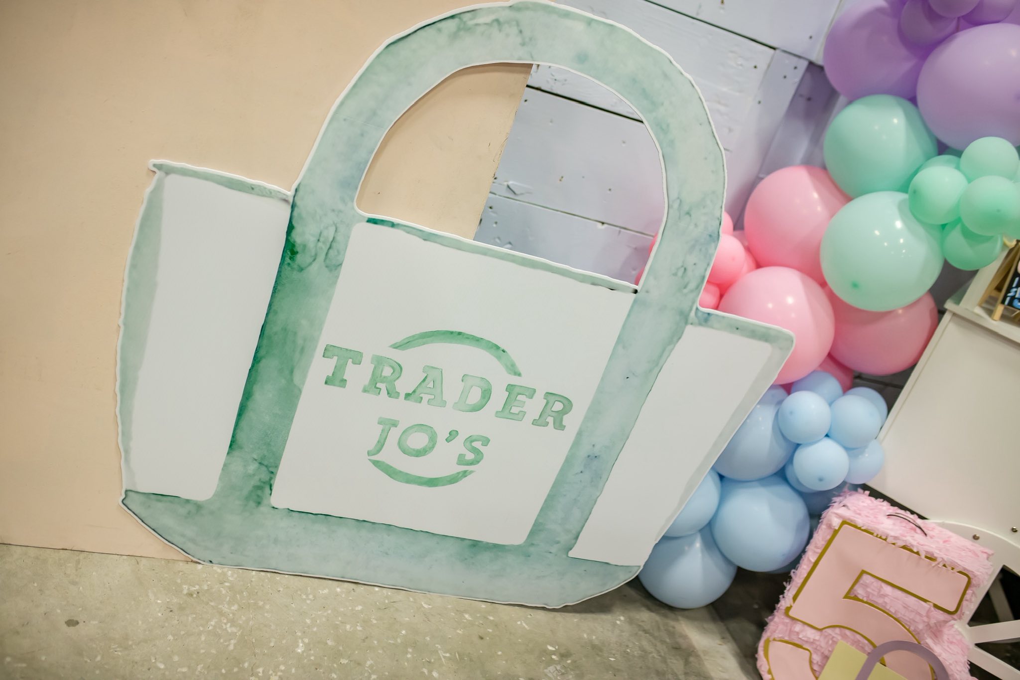 Large cardboard cutout of a green Trader Joe's canvas tote bag standing next to pastel balloon decorations.
