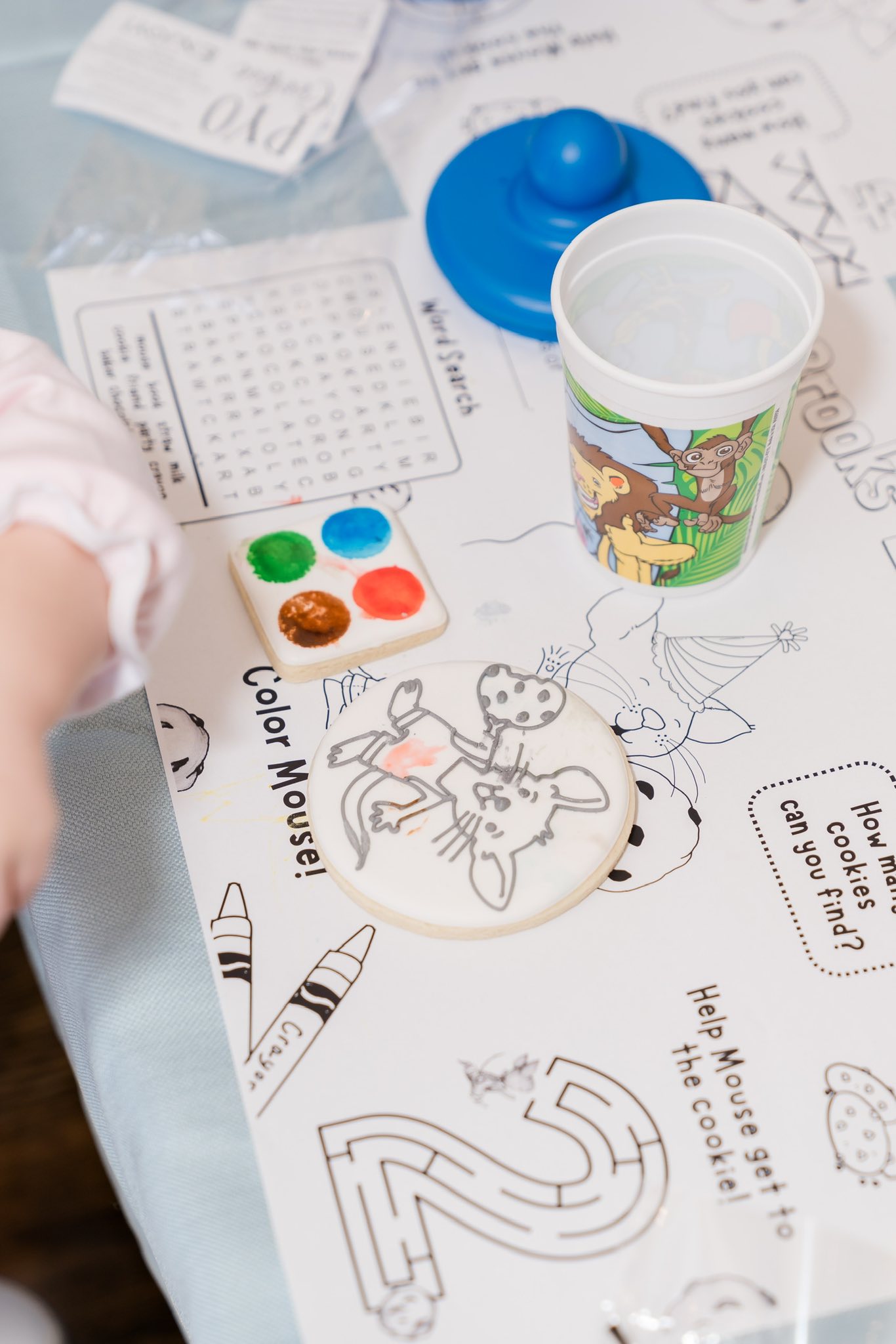 Decorated cookie, paint palette cookie, and water cup on activity placemat for Paint Your Own cookie kit.