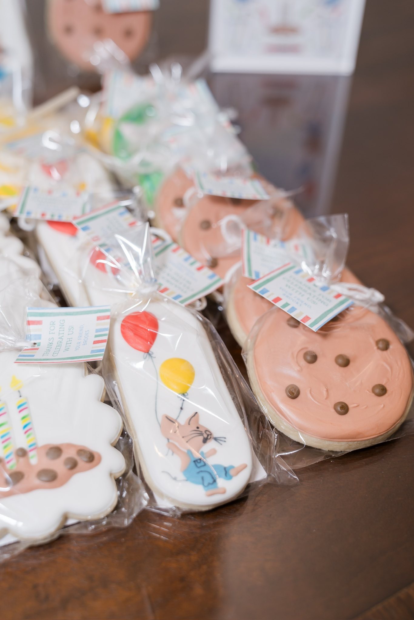Individually wrapped party favor cookies with birthday-themed icing and hanging thank you tags.