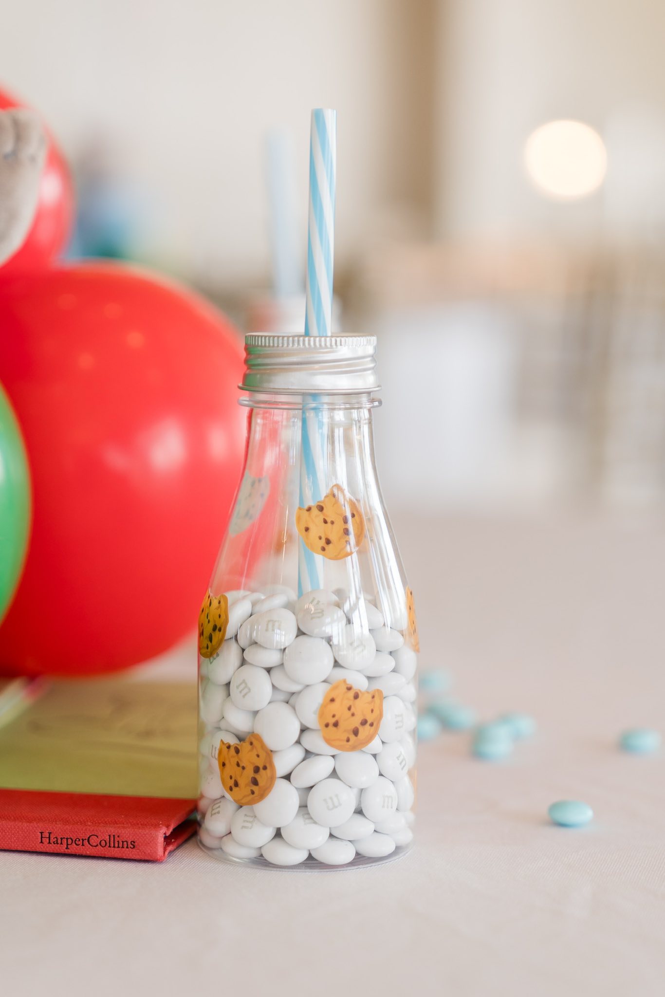 Glass party favor bottle filled with white chocolate candies, decorated with cookie illustrations and a blue striped straw.