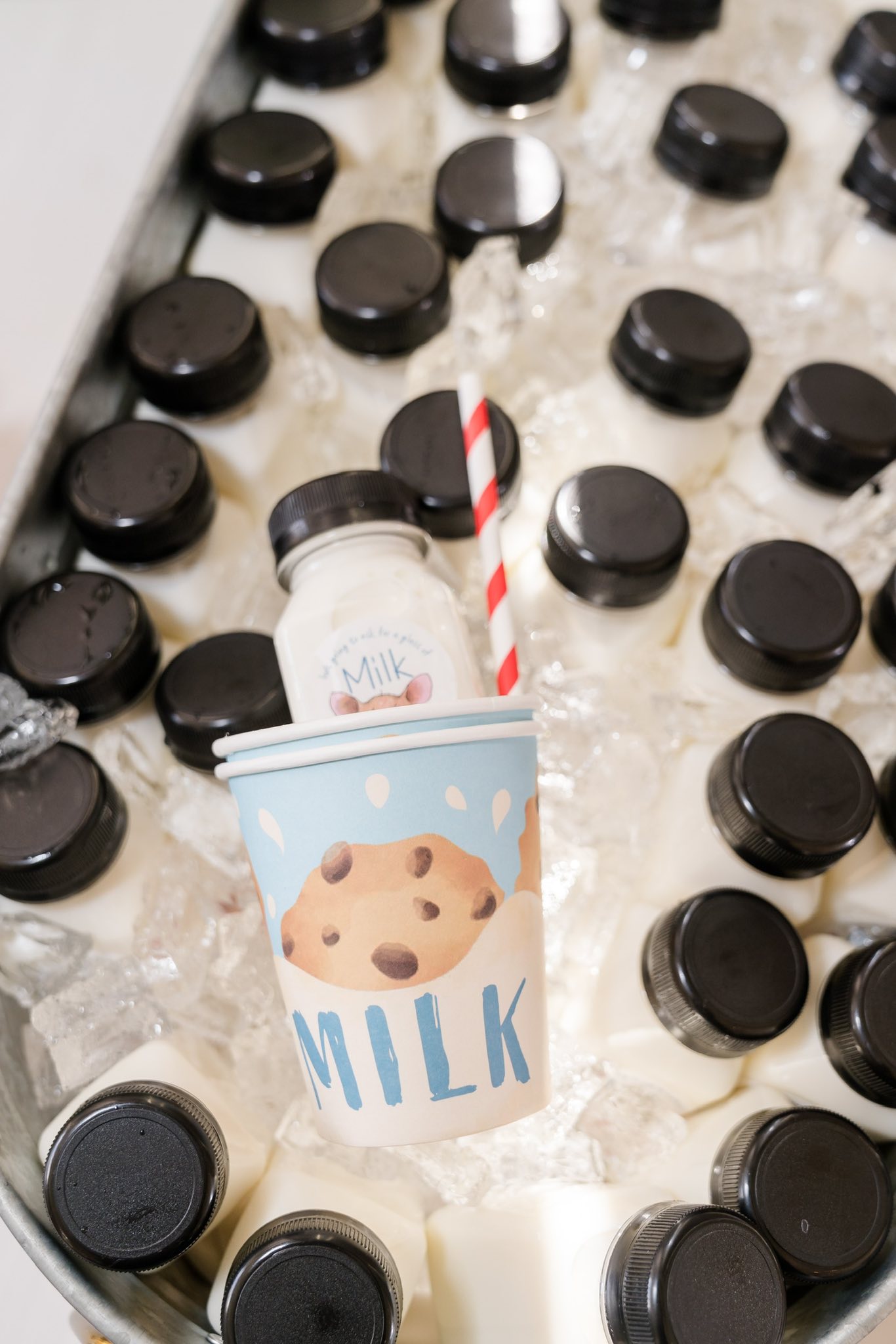 Small bottles of milk on ice with a decorative paper cup featuring a chocolate chip cookie design