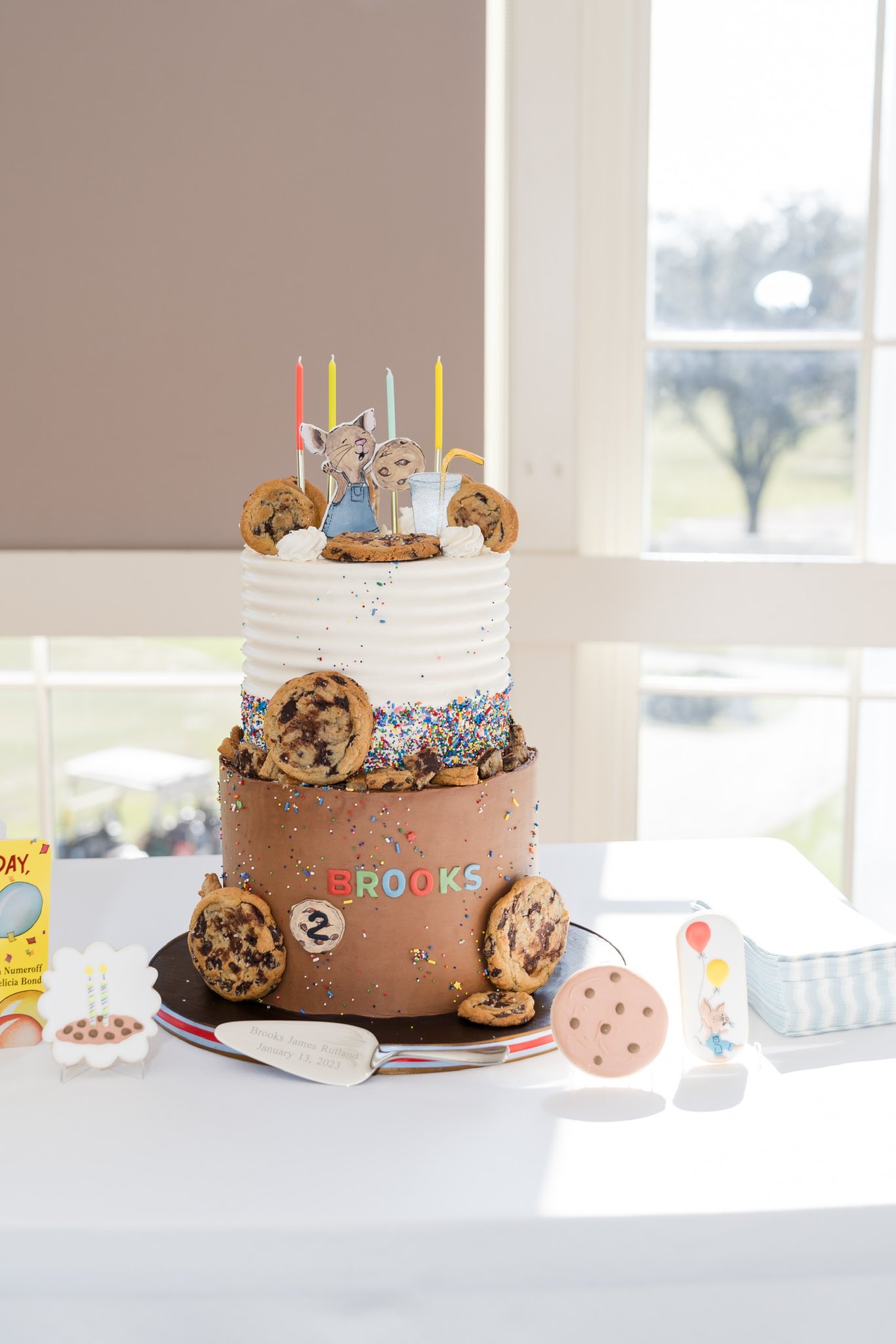 Two-tiered chocolate and white buttercream birthday cake decorated with chocolate chip cookies and a mouse topper.