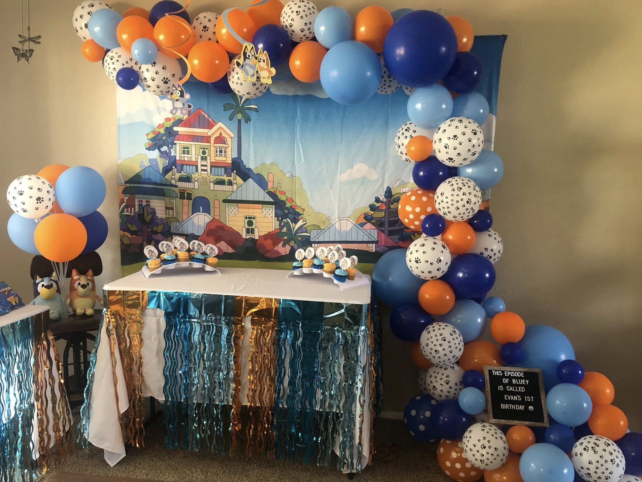 Bluey-themed first birthday party setup with balloon arch, backdrop, and cupcake display.