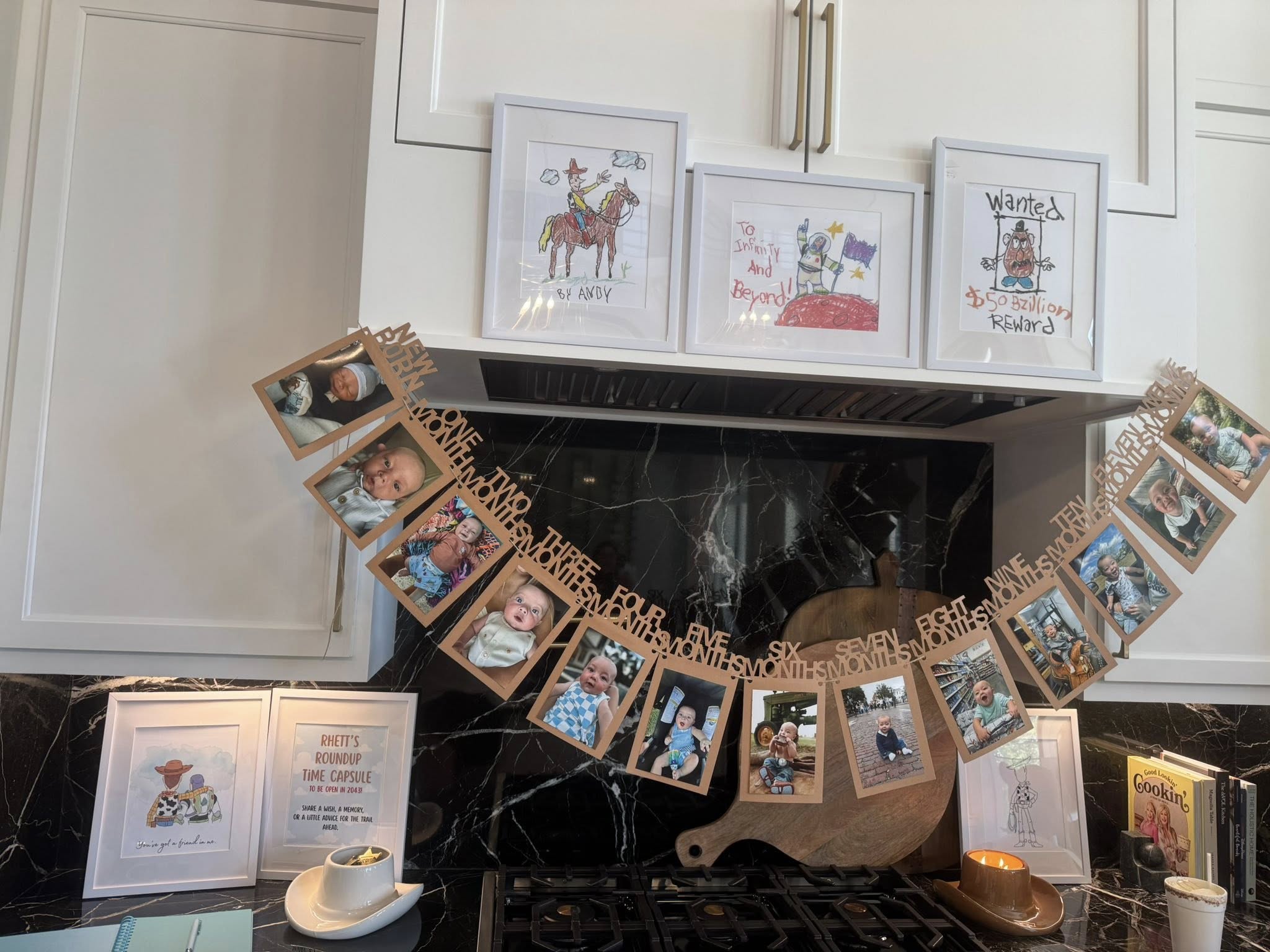 A monthly baby milestone photo banner displayed above a kitchen stove with Toy Story themed wall art.