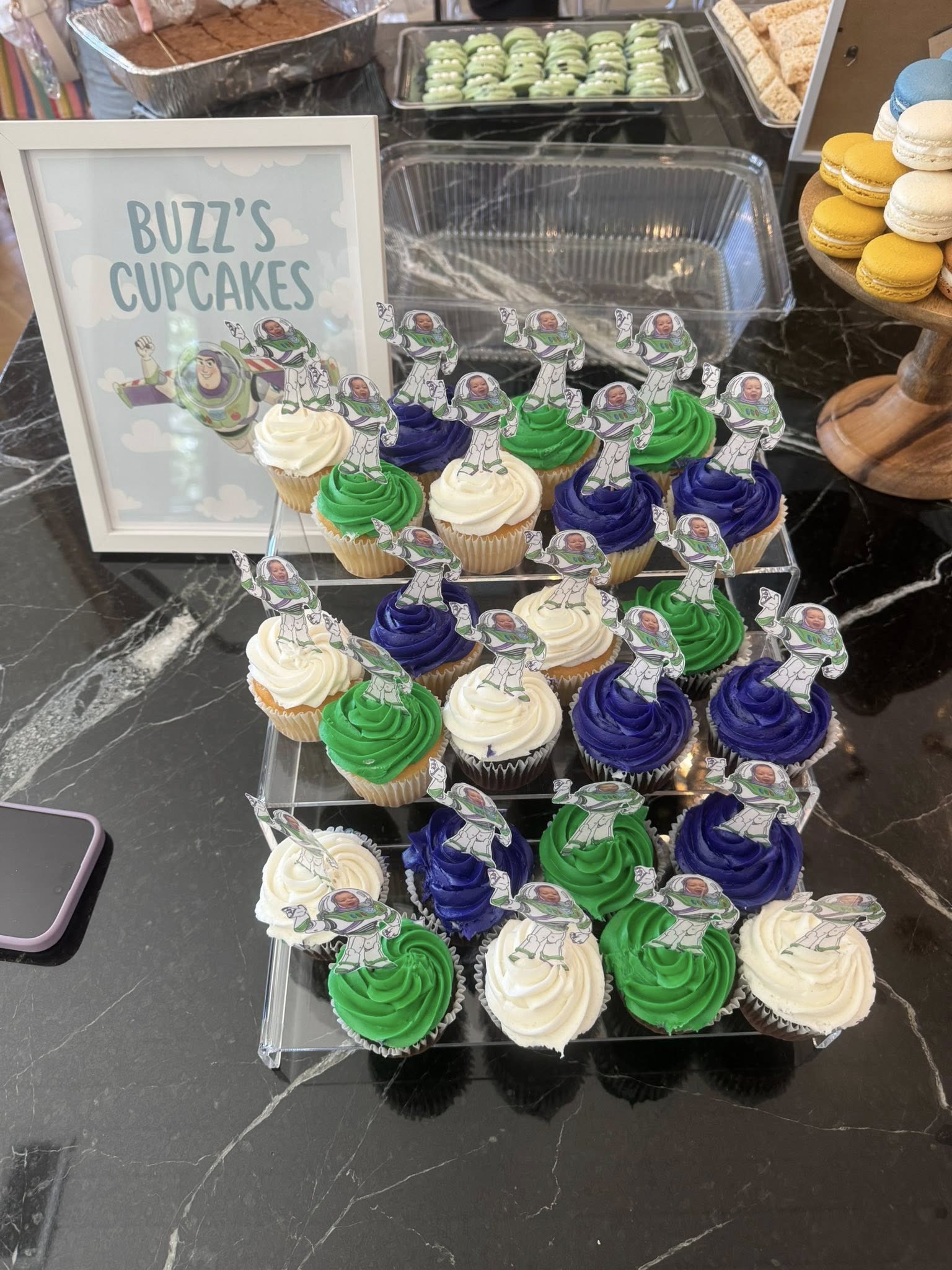 Cupcakes decorated with green, white, and purple frosting, each featuring a custom Buzz Lightyear cake topper.