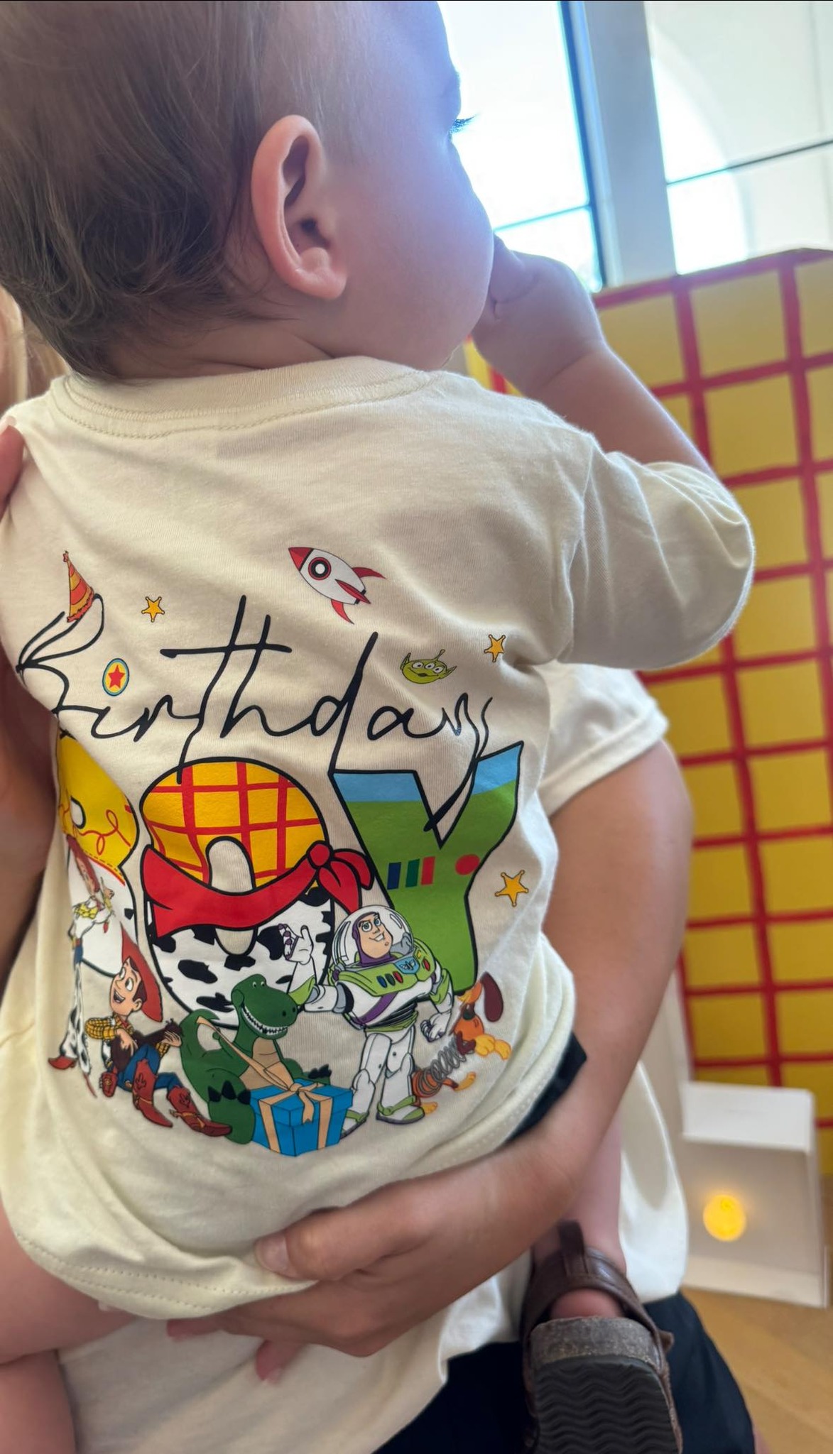 Toddler wearing a cream-colored Toy Story-themed birthday boy t-shirt.