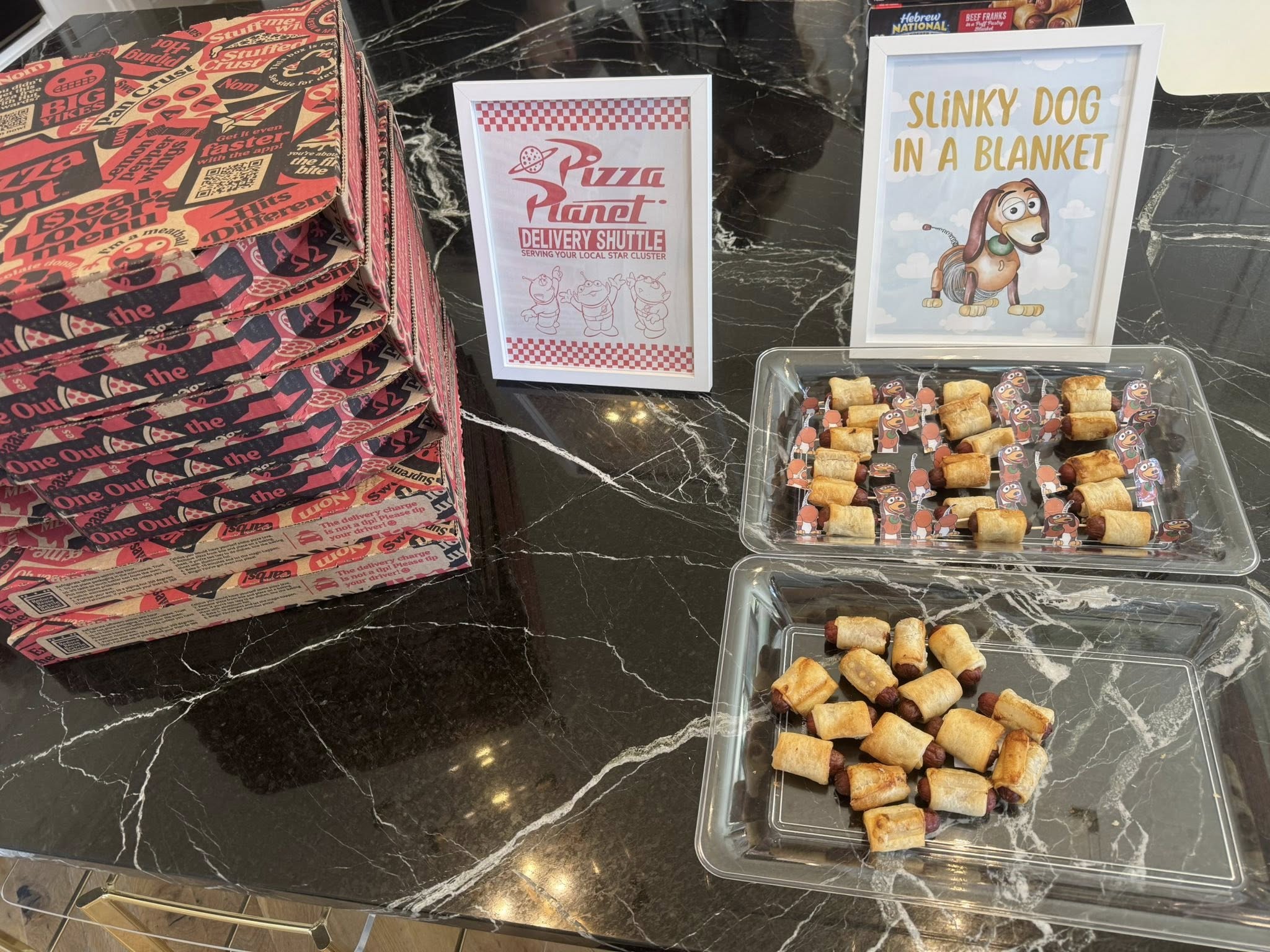 Slinky Dog in a Blanket appetizer display with a themed sign and a stack of Pizza Planet pizza boxes.