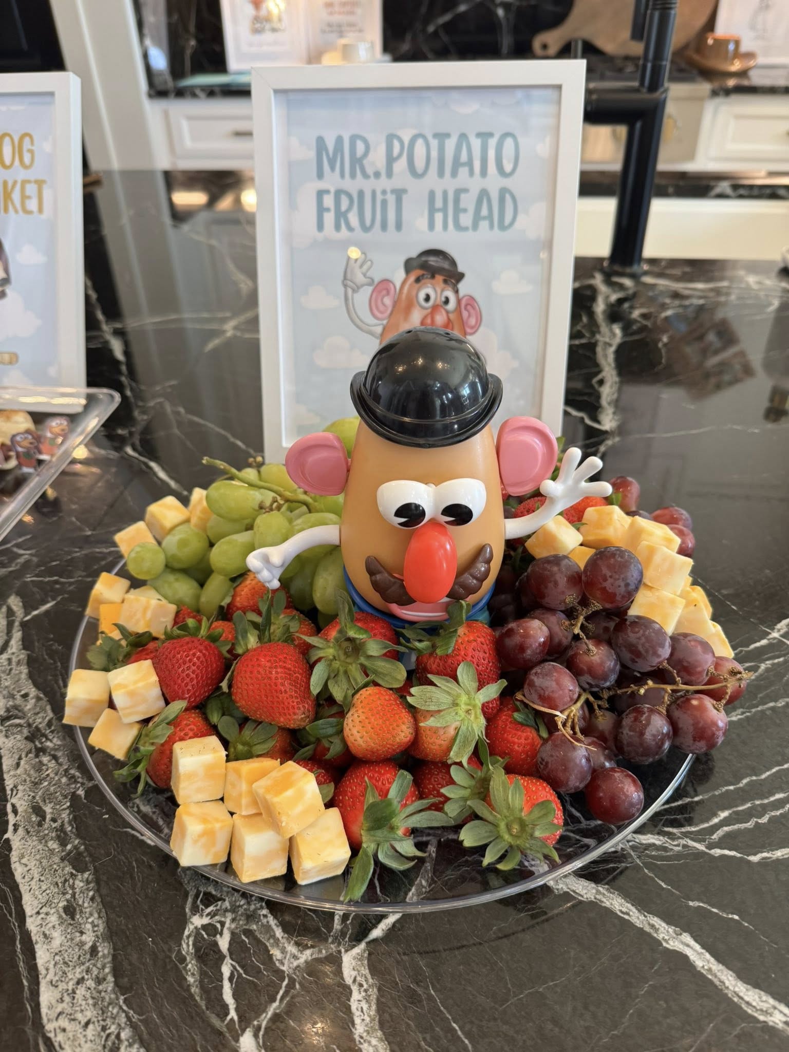 Mr. Potato Head figure decorating a platter of fresh strawberries, grapes, and cubed cheese.
