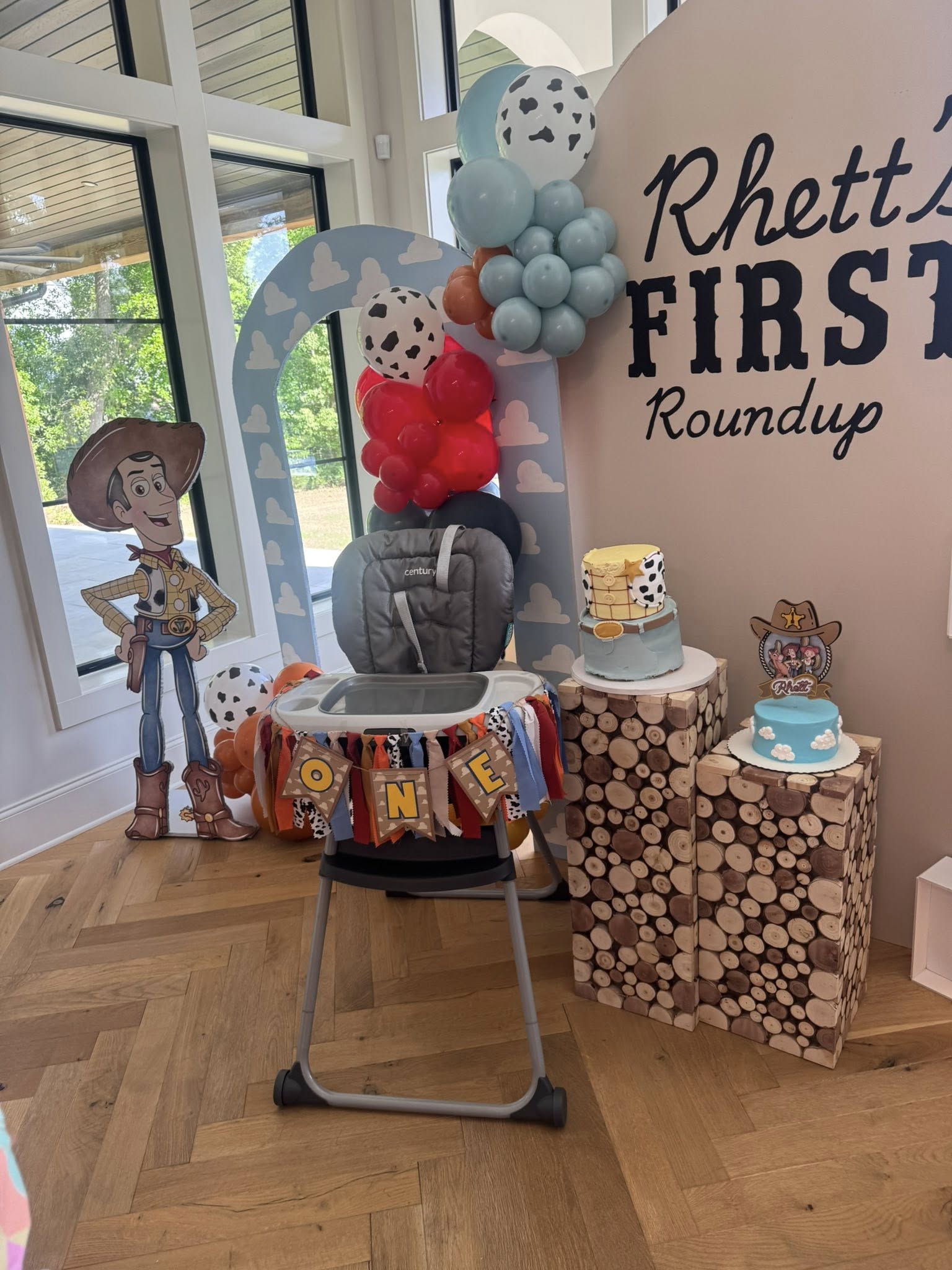 Toy Story inspired first birthday party decor featuring a woodsy high chair, balloon arch, and customized cakes.
