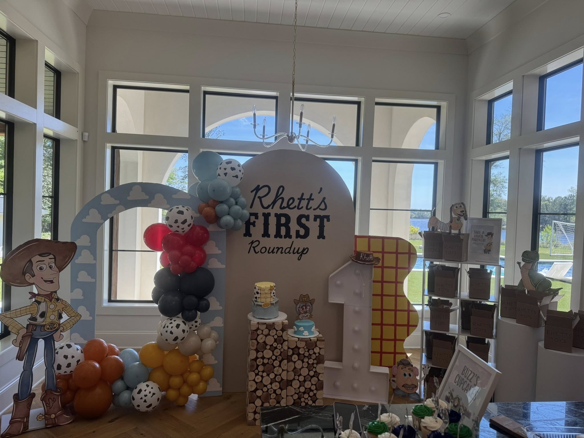 Toy Story inspired first birthday party decor with a balloon arch, a wood-patterned '1', and Rhett's Roundup sign.