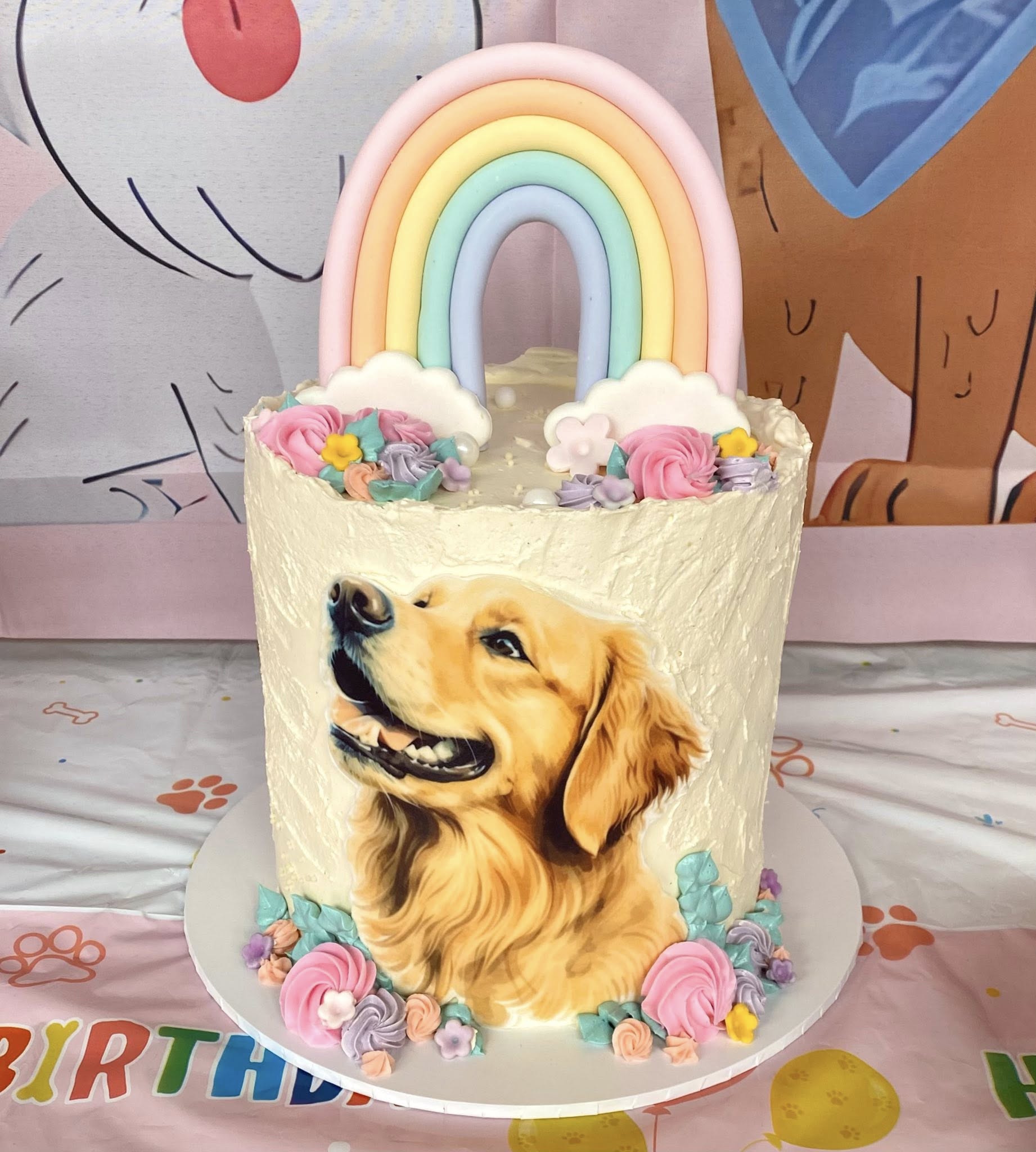 Birthday cake decorated with a Golden Retriever portrait topped with a pastel rainbow and frosting flowers.