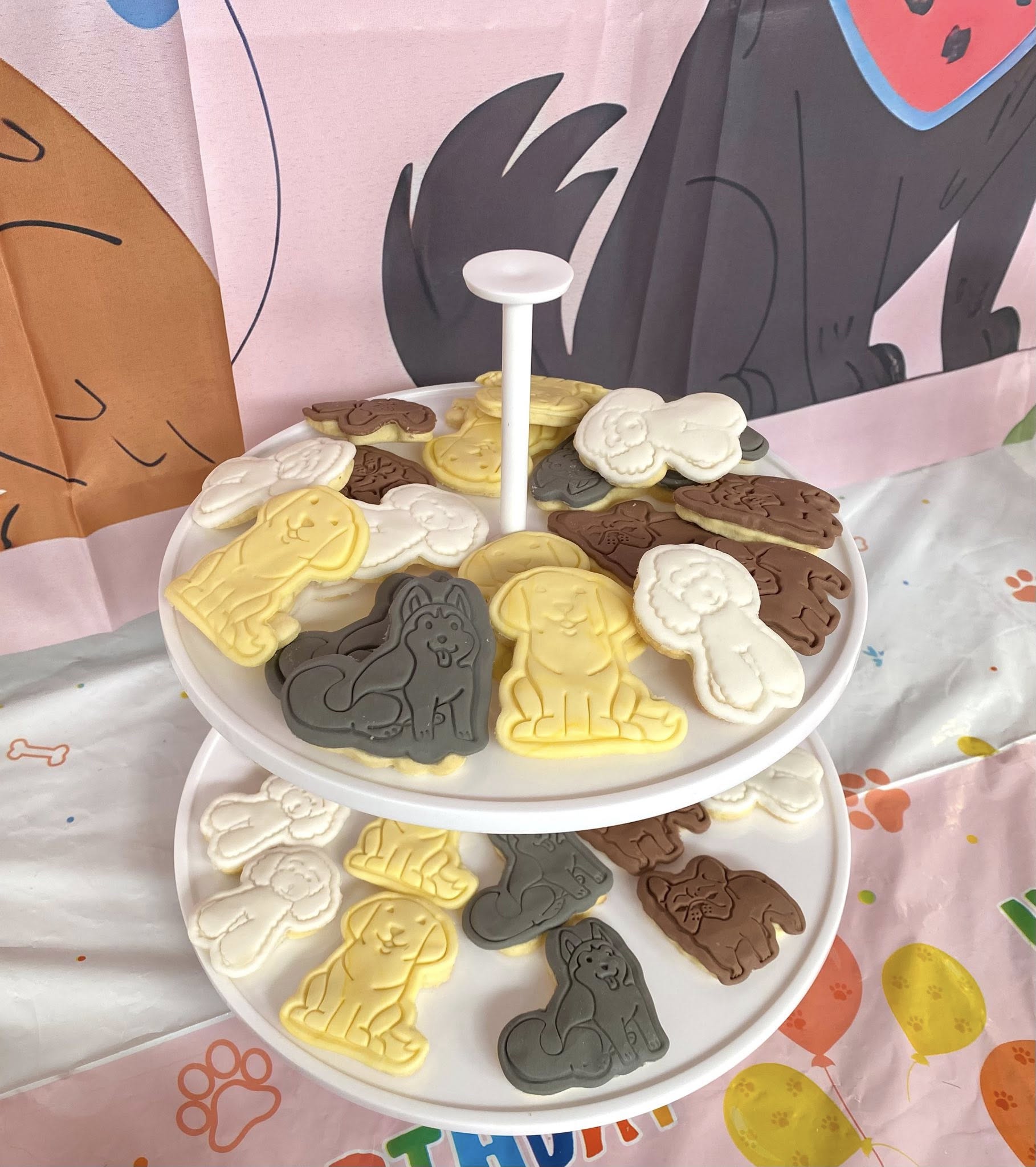 Two-tiered display stand featuring assorted dog-shaped cookies in white, chocolate, and golden colors.