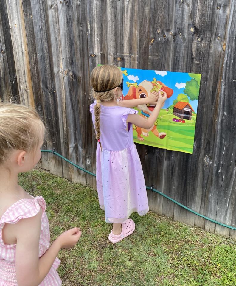 Girl wearing a blindfold playing a pin the bone on the puppy party game