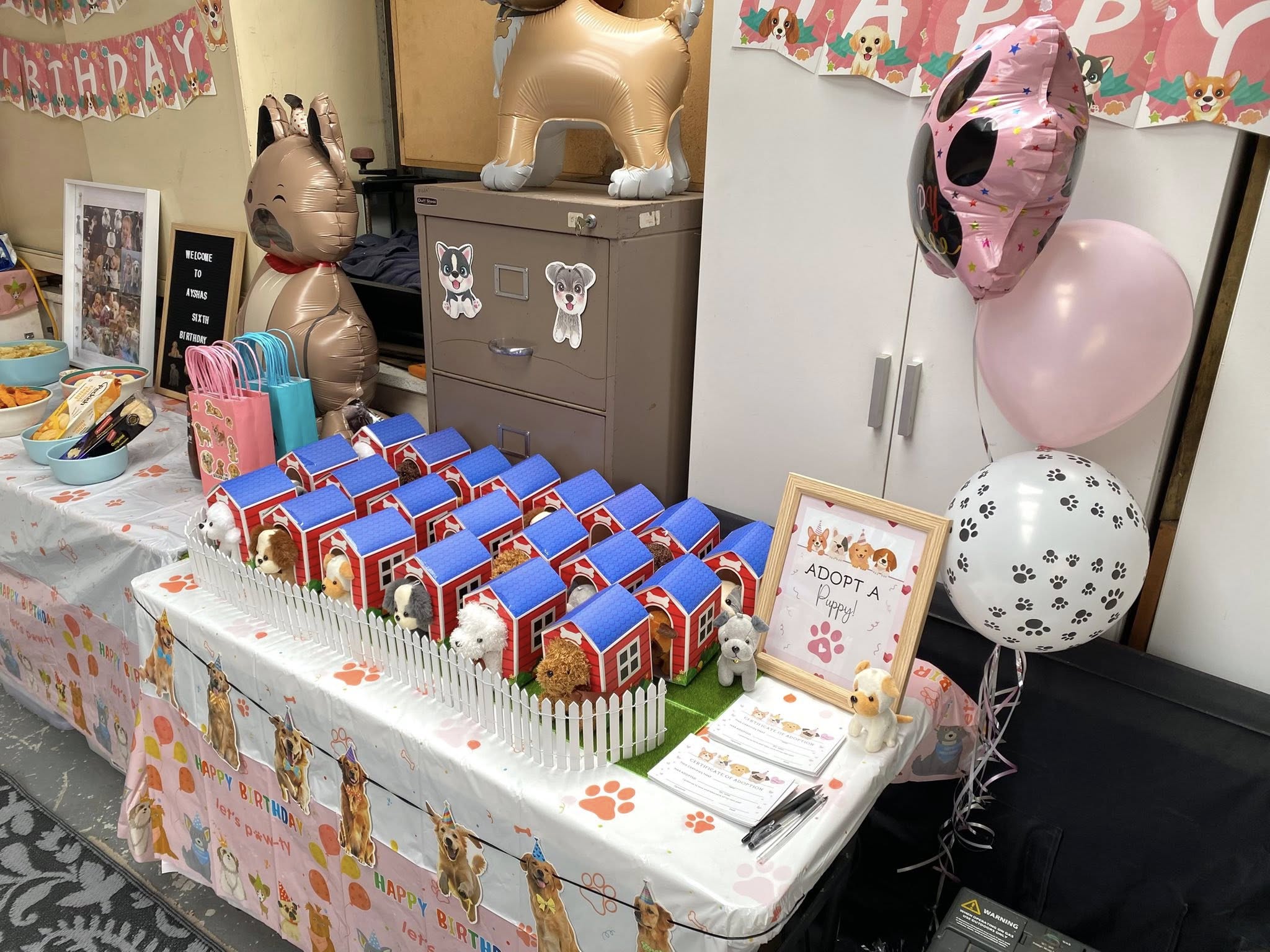 Puppy adoption party favor display with plush dogs in small red doghouses sitting on a table.