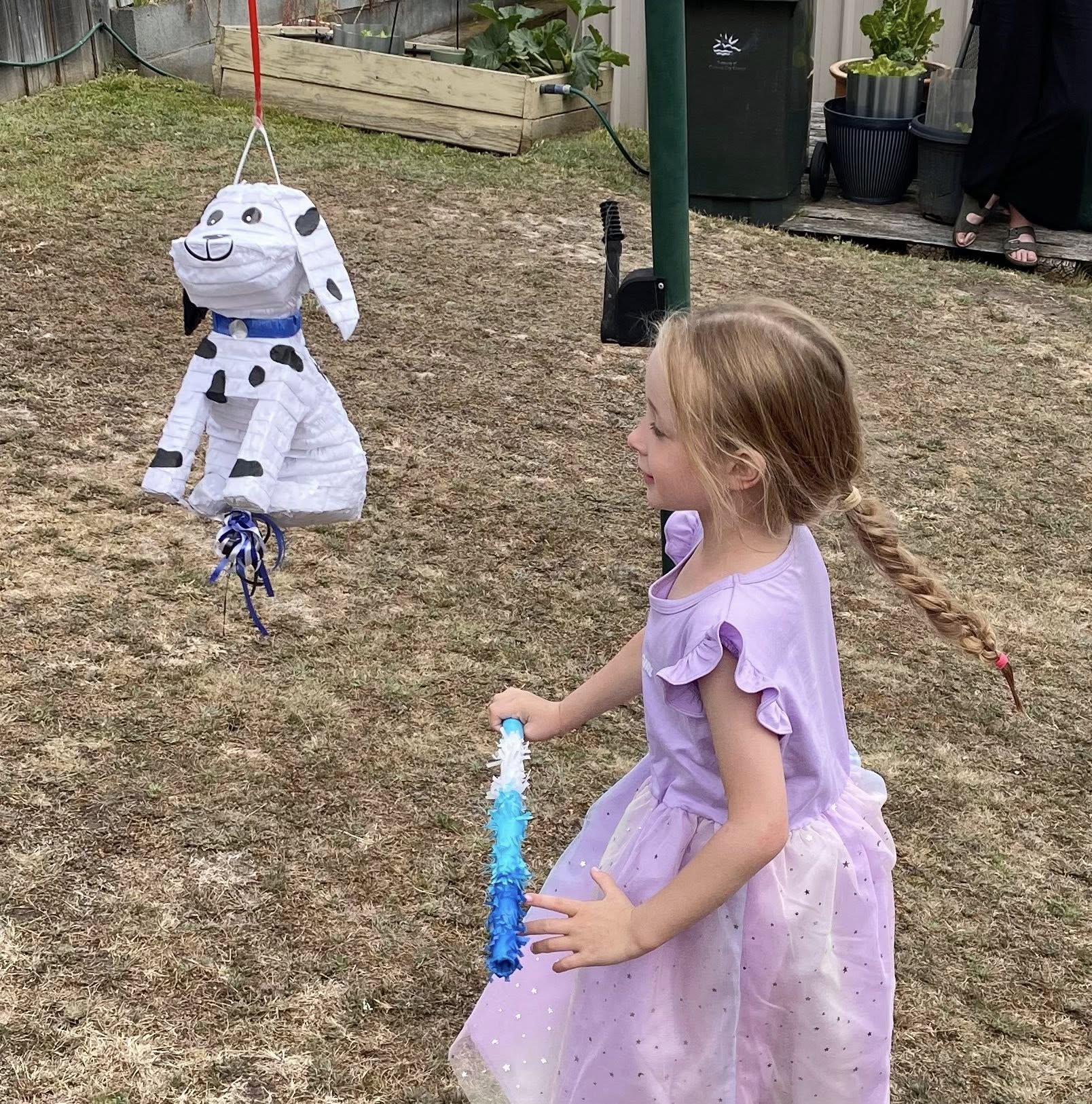 Young girl in a purple dress about to hit a dalmatian-shaped piñata with a stick