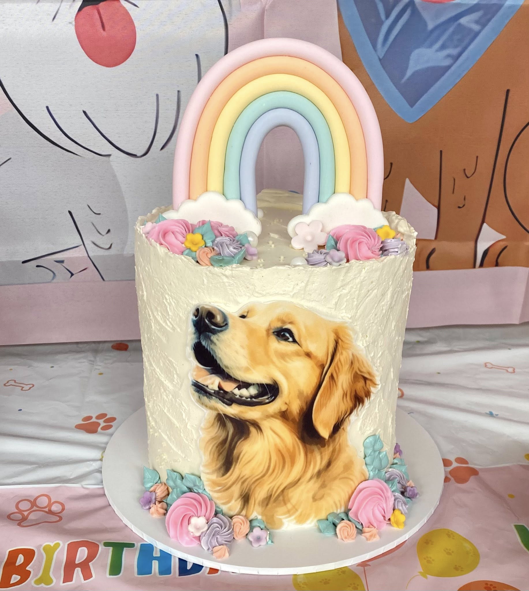 Custom birthday cake featuring a golden retriever portrait, topped with a fondant rainbow and floral decorations.