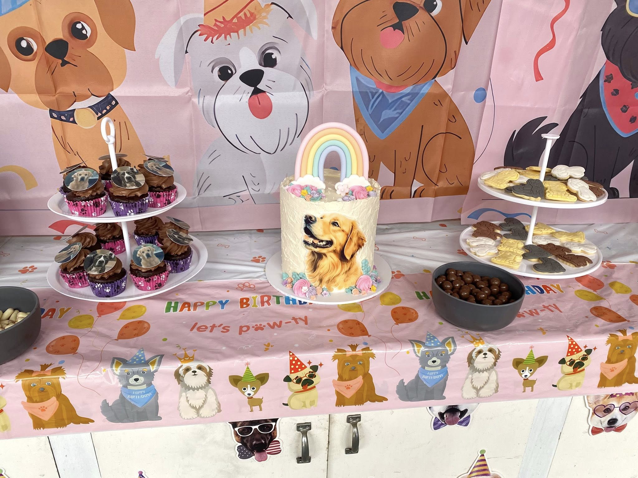 Dog-themed birthday party table with a golden retriever cake, dog-topped cupcakes, and paw-shaped treats.
