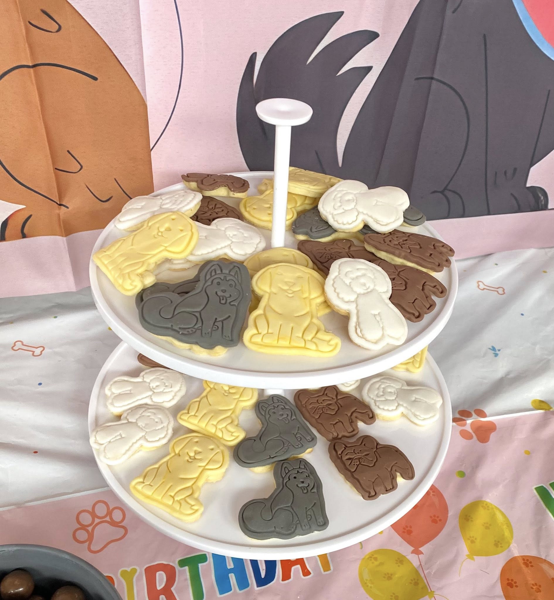 Two-tiered stand filled with various dog-shaped cookies in shades of brown, white, and yellow