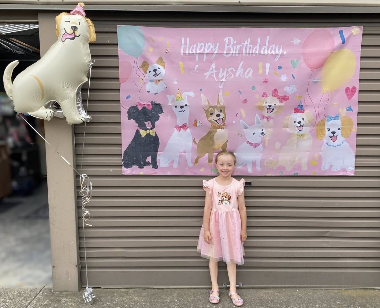 Young girl standing in front of a pink dog-themed birthday backdrop with a matching dog balloon.