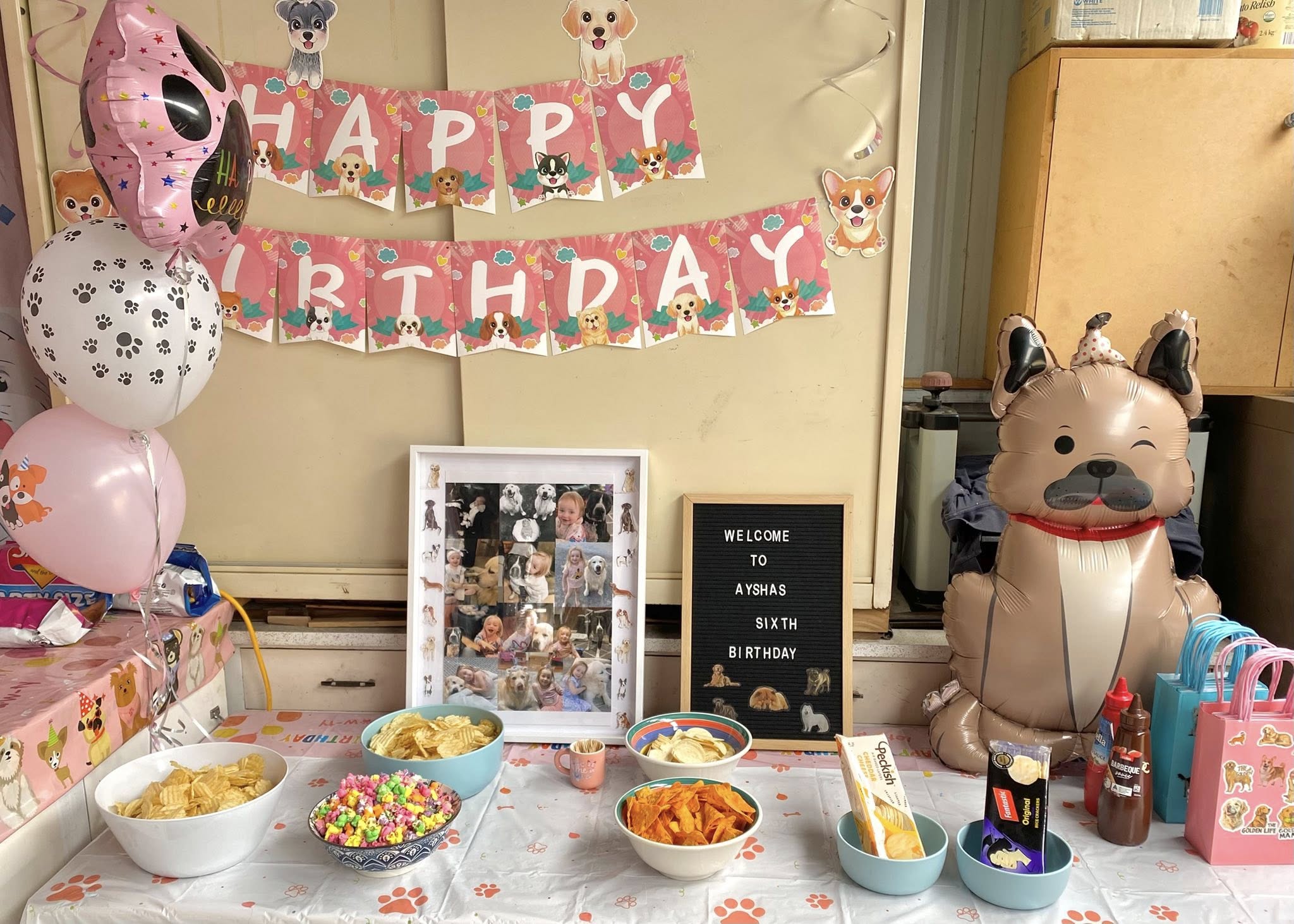 Puppy-themed birthday party decorations with a Happy Birthday banner, dog balloons, snacks, and a photo collage.