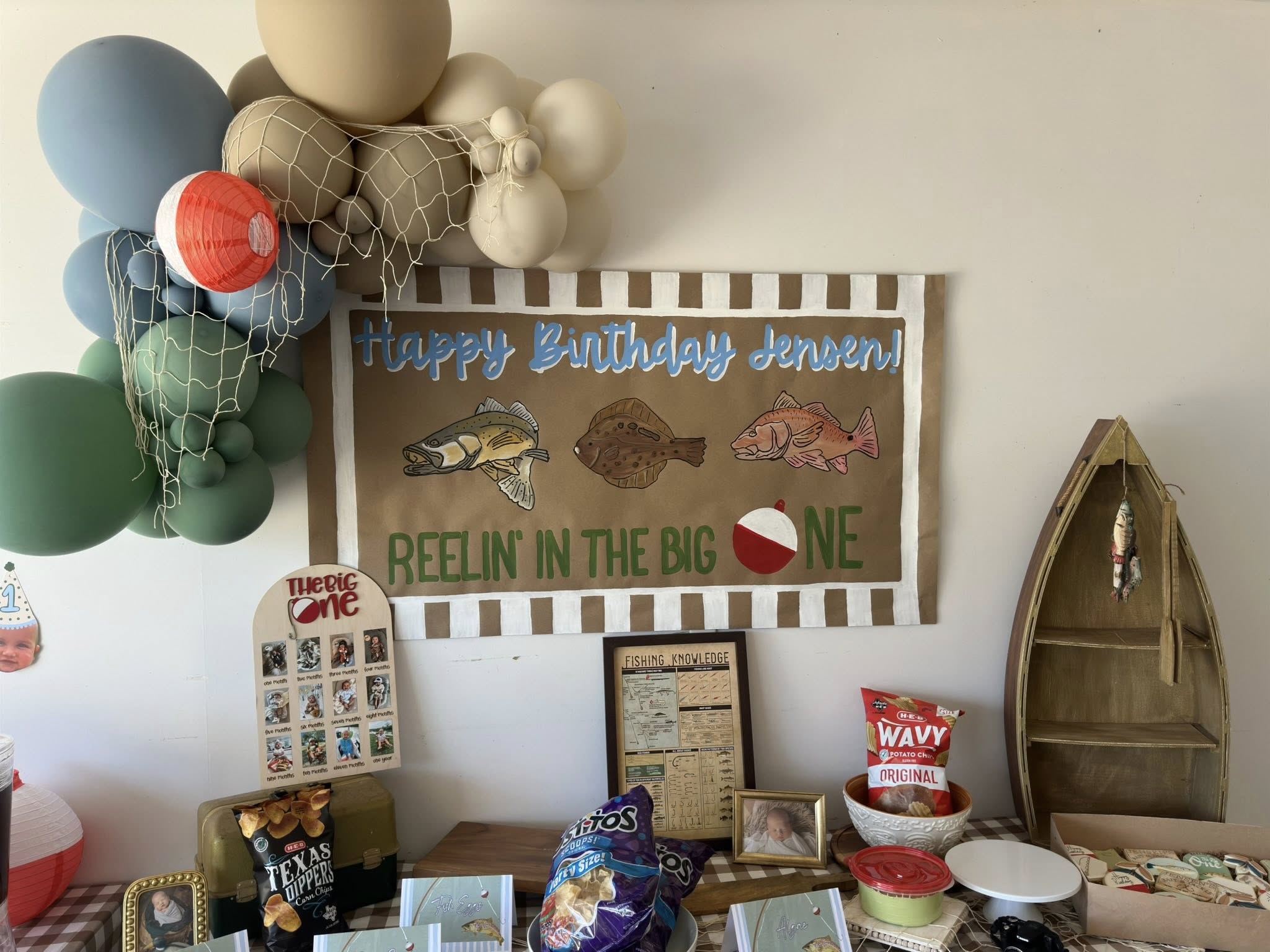 Fishing-themed first birthday party display with personalized banner, balloons, and snacks.