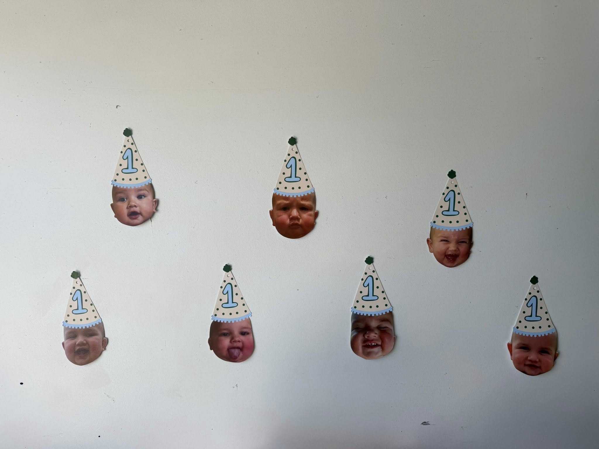 Seven custom cutouts of a baby's face wearing a blue polka-dot party hat with the number 1 for a first birthday