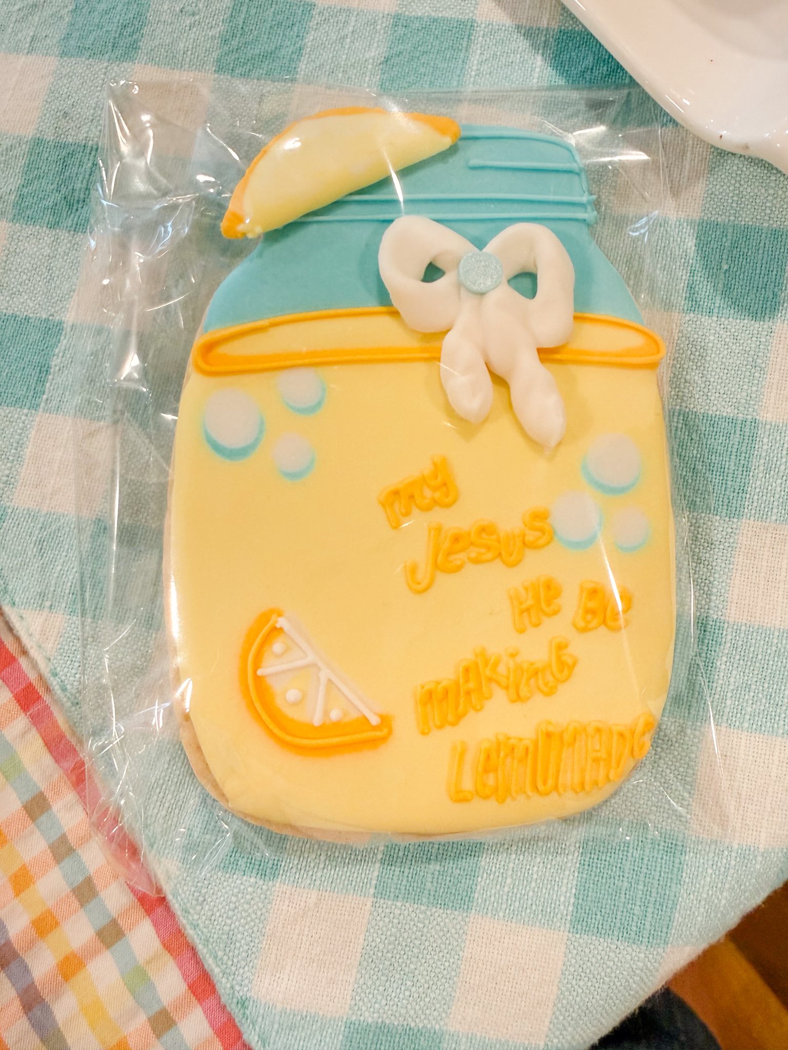 Mason jar shaped sugar cookie decorated with yellow icing, a lemon slice, a white bow, and the text My Jesus He Be Makin Lemonade.