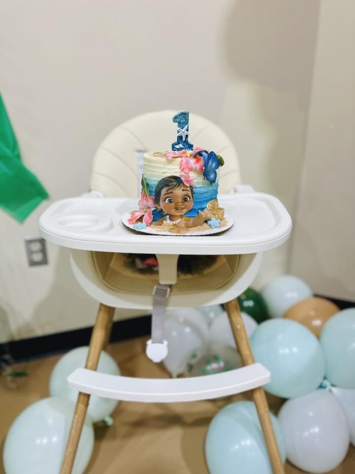Moana-themed first birthday cake on a white high chair surrounded by balloons