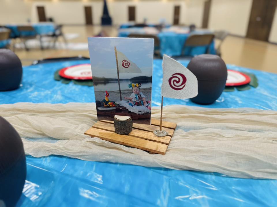 Moana-themed birthday party centerpiece with a photo of a toddler and a miniature boat flag.
