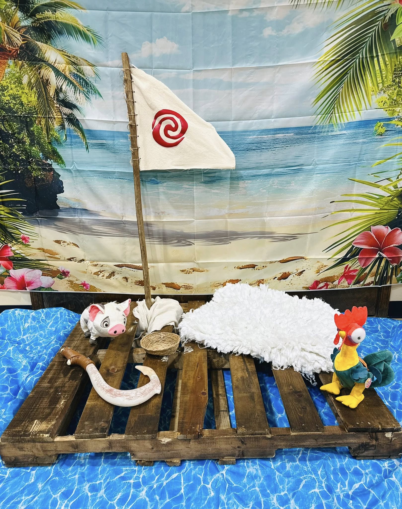 Moana themed party decoration featuring a wooden pallet boat with Pua the pig, Hei Hei the rooster, and Maui's hook