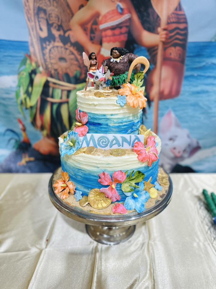Two-tier Moana-themed birthday cake decorated with tropical flowers and ocean-inspired blue icing.