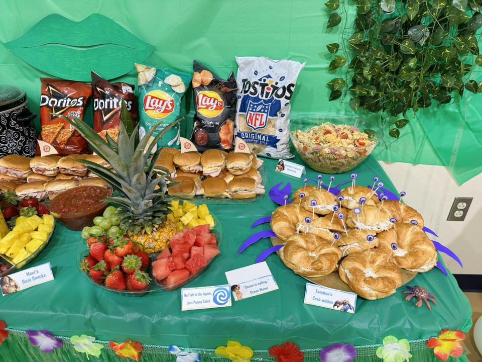 A party buffet table featuring snacks and sandwiches decorated in a Moana-themed ocean style.