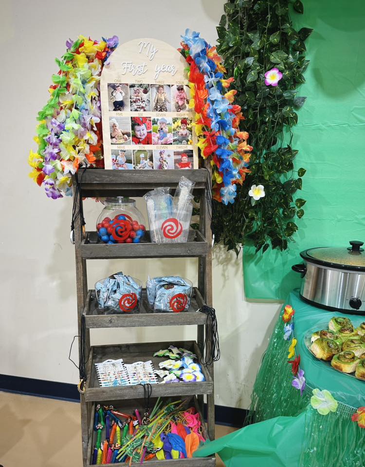 Moana themed party display stand with a baby milestone photo board, party favors, and floral garlands.