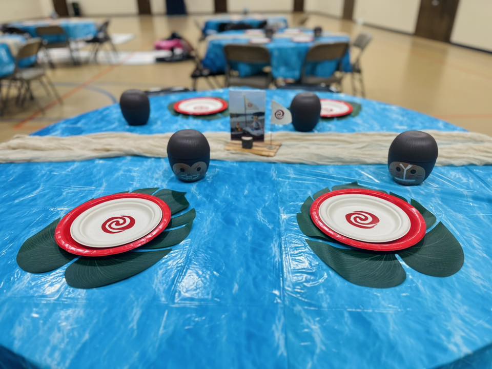 Moana-themed event table setting with tropical decor, blue tablecloths, and custom plates.