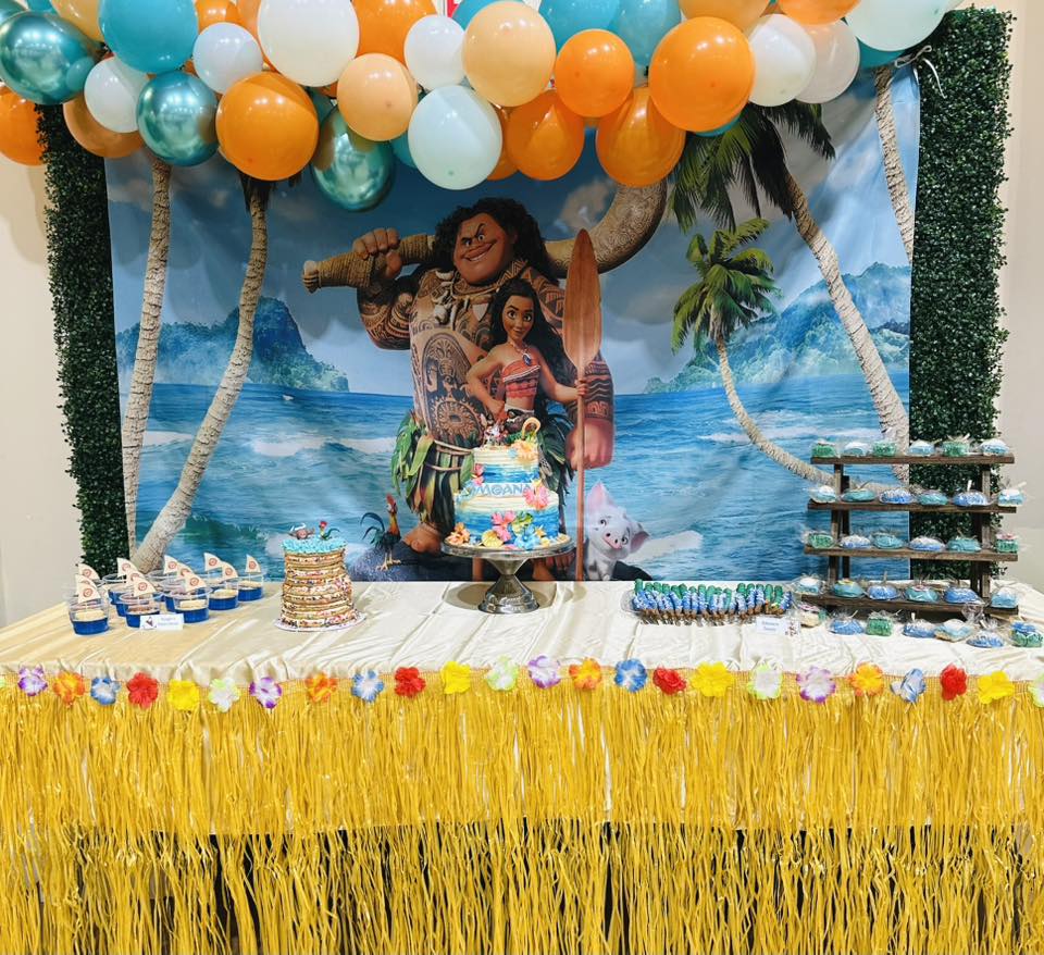 Moana themed party dessert table with a Moana birthday cake, tropical decorations, and a balloon garland.