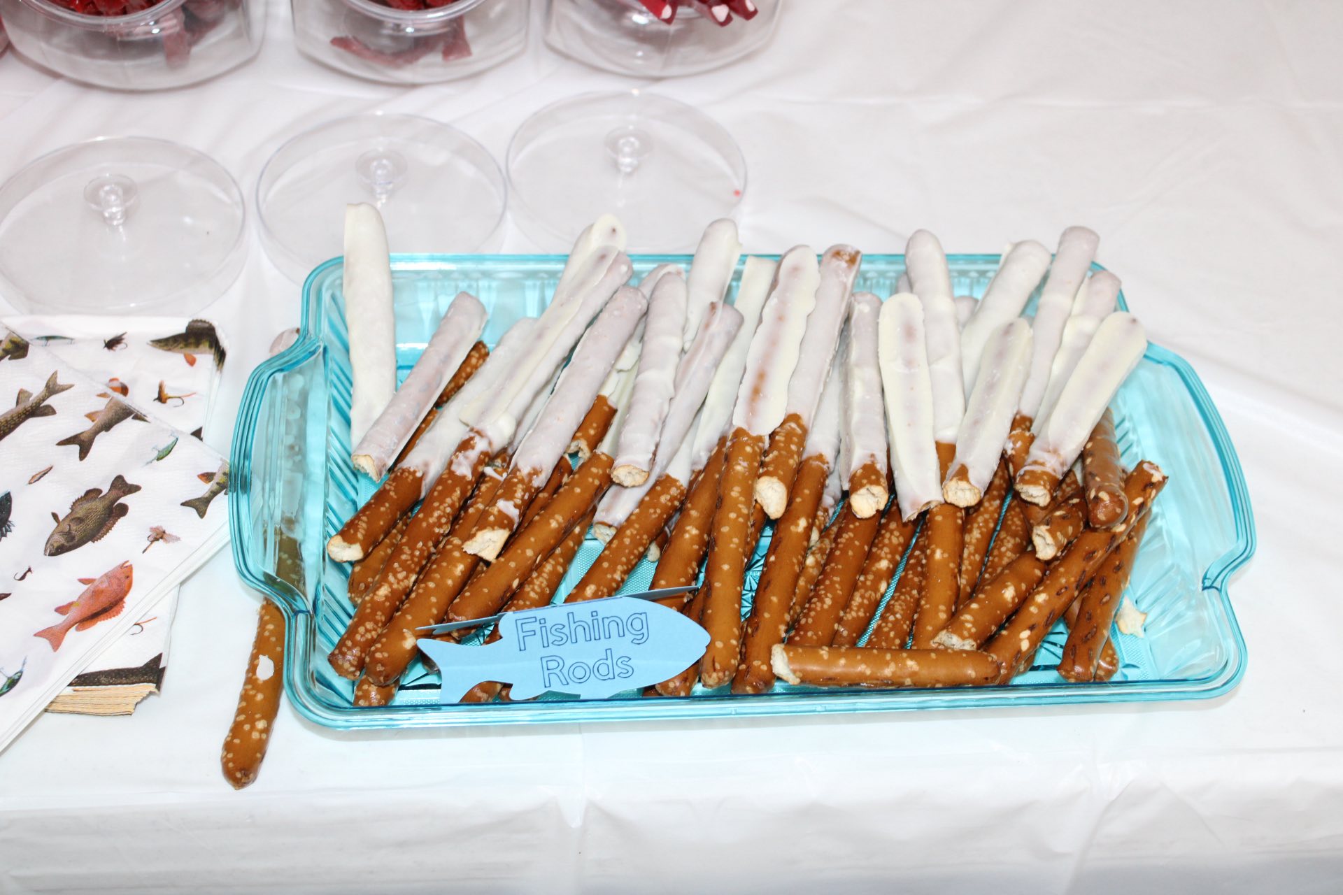 White chocolate-dipped pretzel rods labeled as Fishing Rods in a blue serving tray