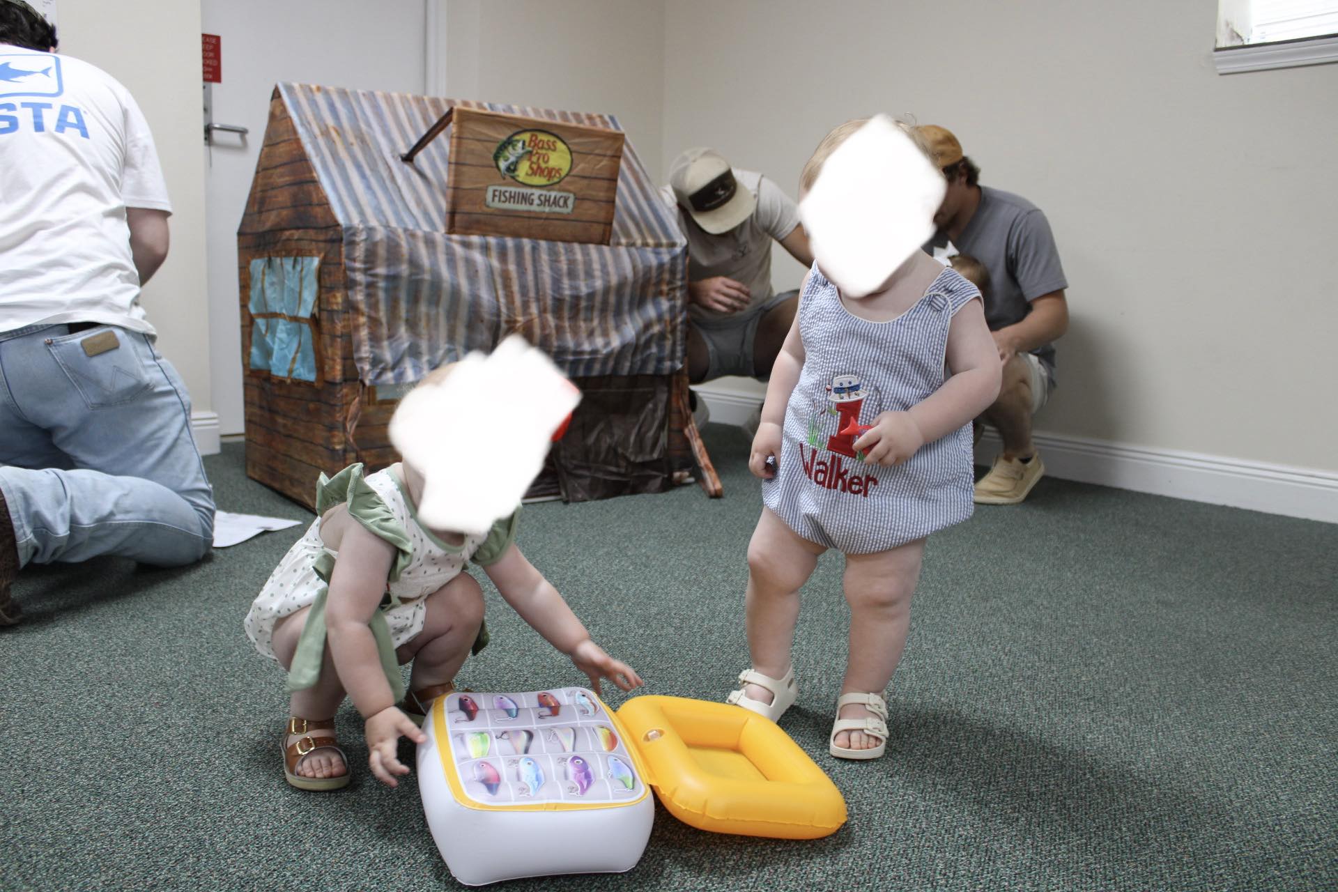 Two young children playing with an inflatable fishing toy set in front of a Bass Pro Shops Fishing Shack playhouse