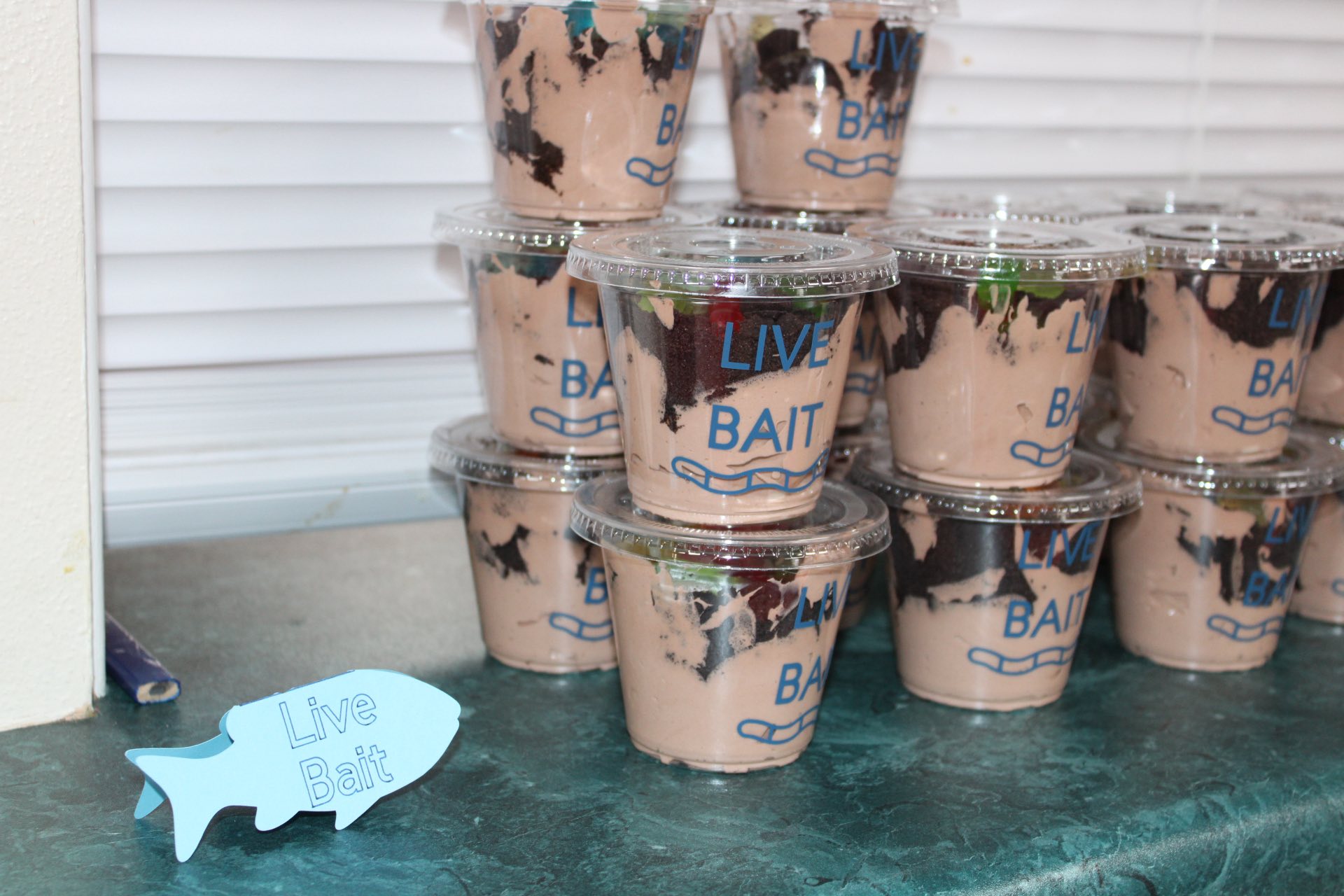 Clear plastic cups filled with dirt pudding layered like live bait with a small fish-shaped sign.