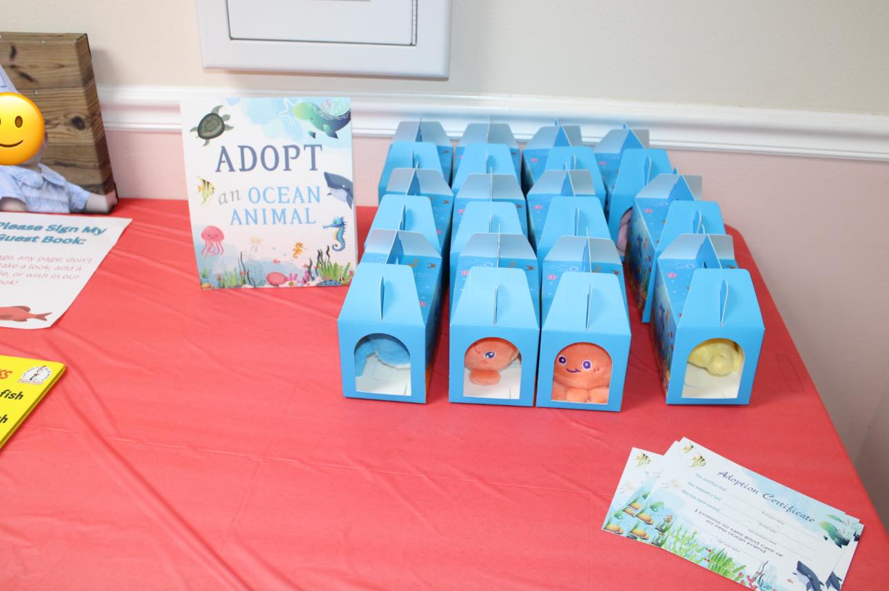 Adopt an ocean animal station at a party with blue treat boxes containing plush toys and adoption certificates.
