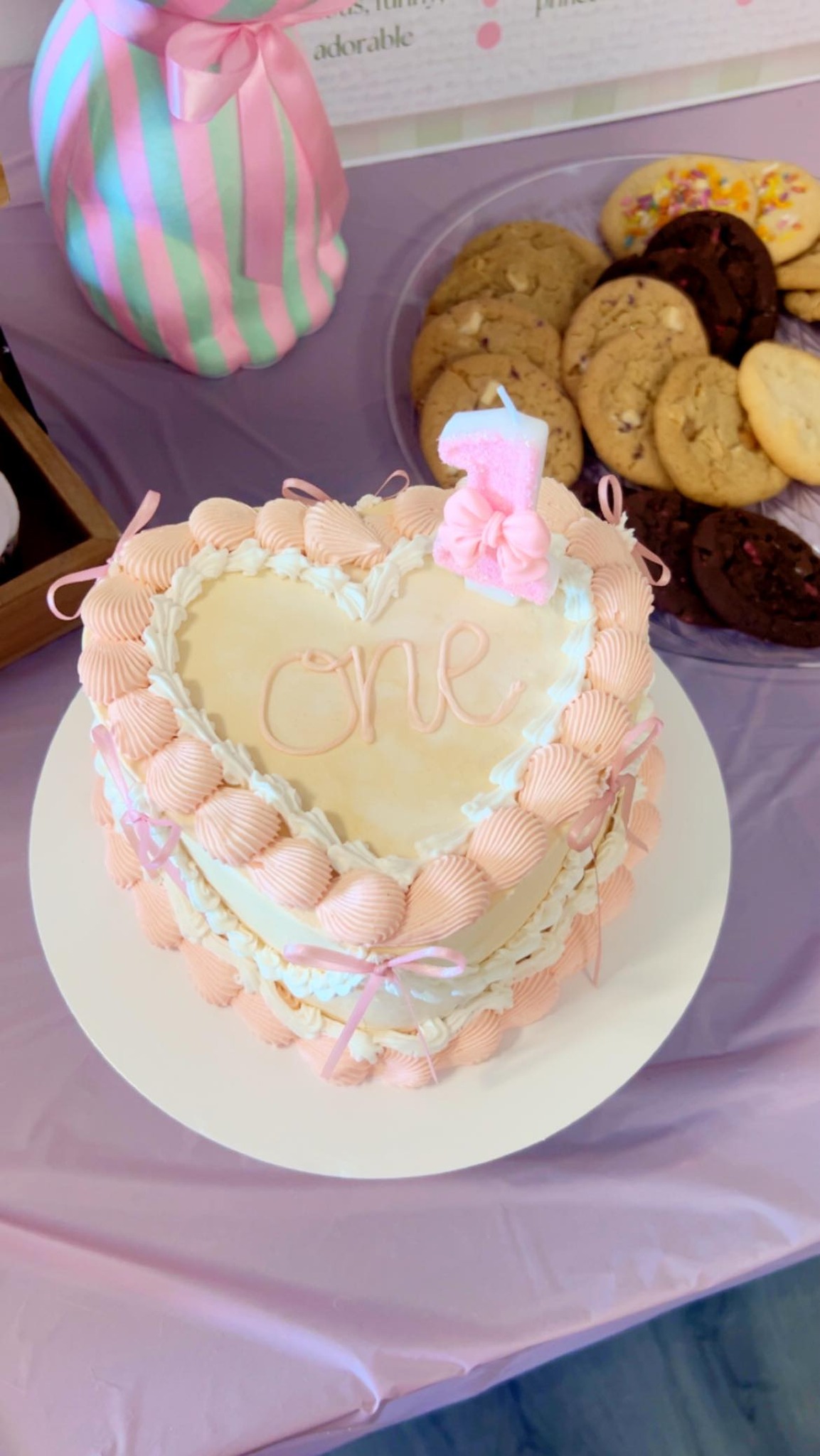 Heart-shaped first birthday cake with light pink frosting, a number one candle, and ribbon decoration