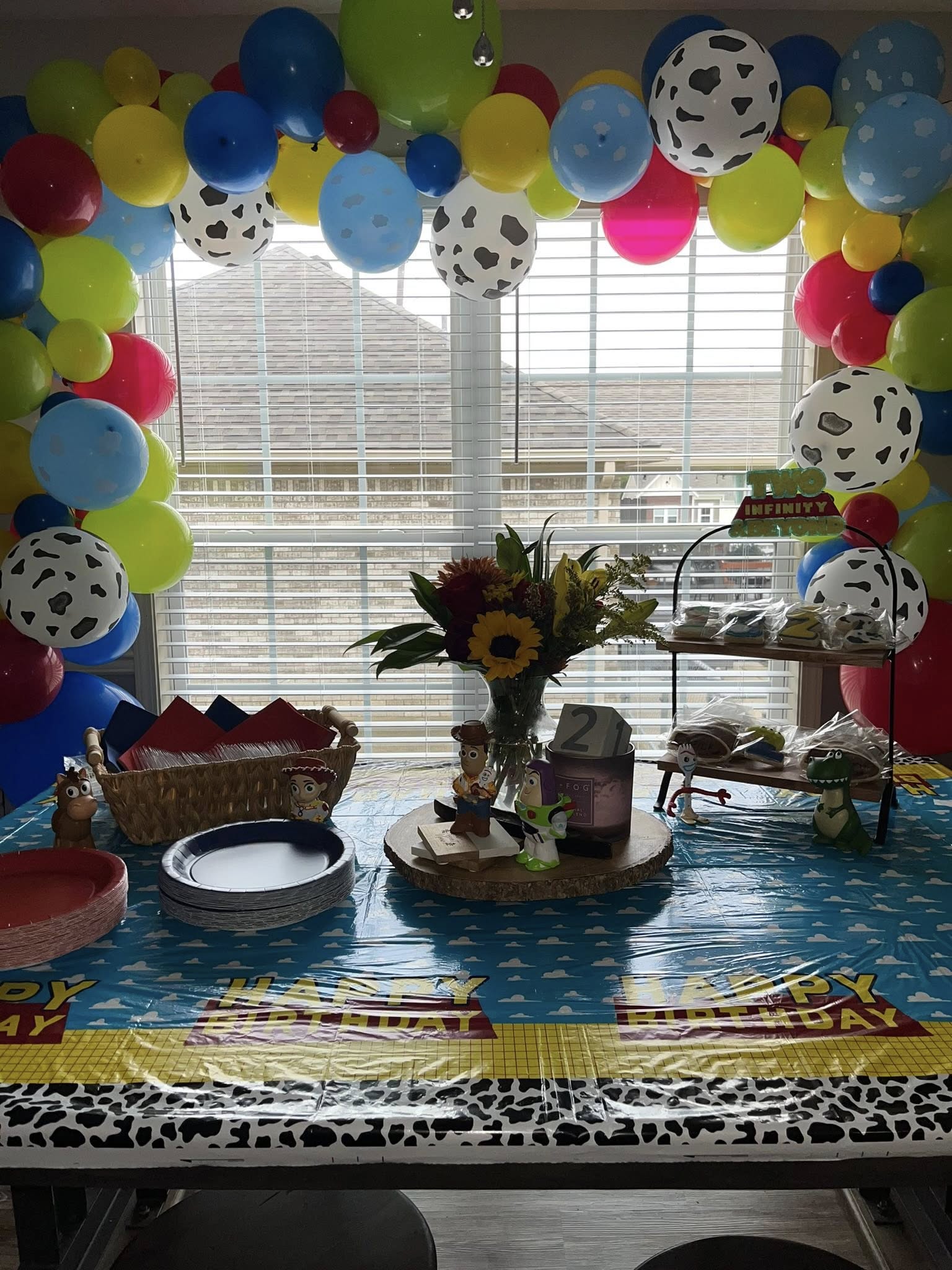 Toy Story themed birthday party table with balloon arch, character figurines, and party supplies.