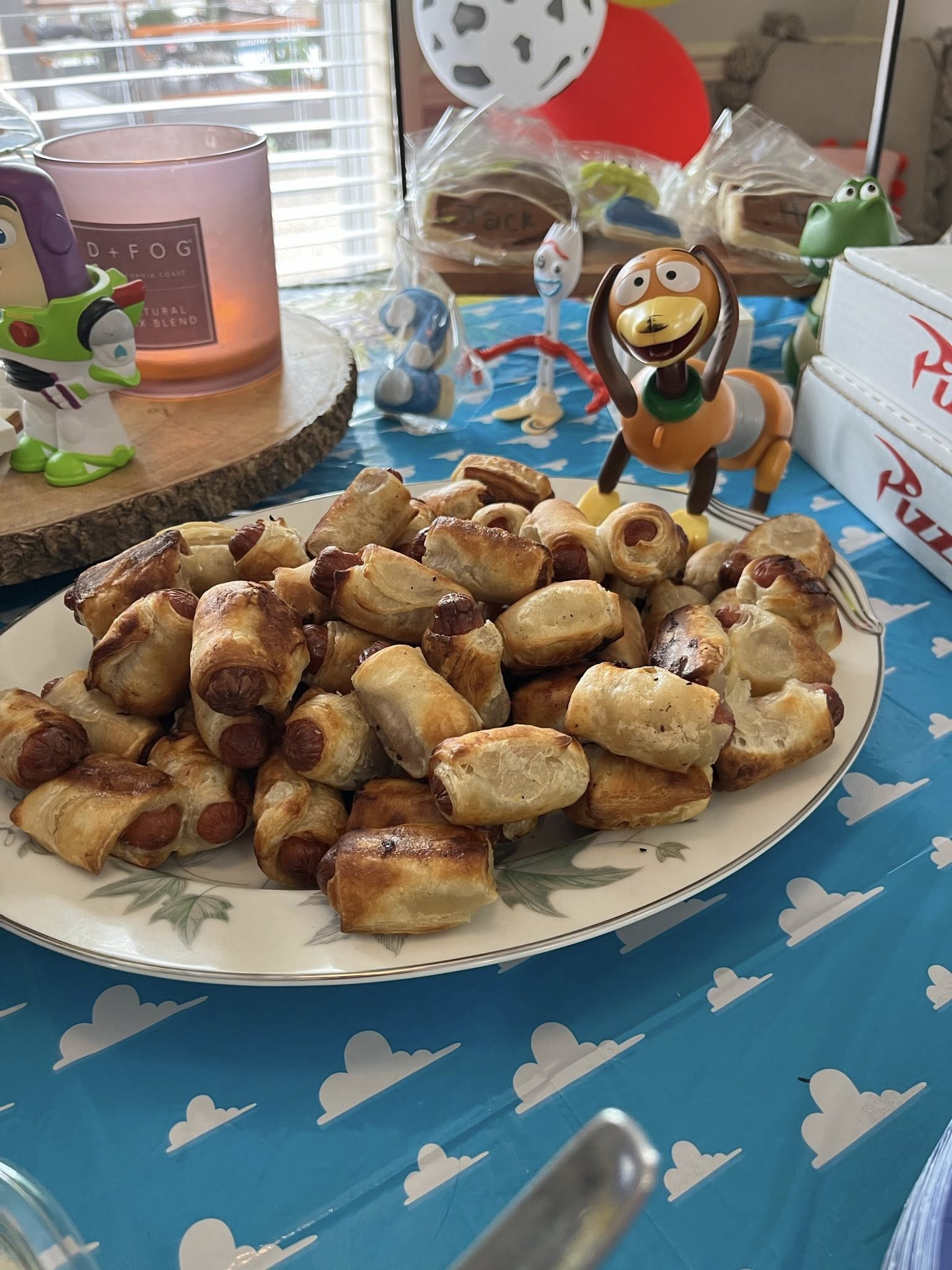 A platter of golden-brown pigs in a blanket on a Toy Story themed party table.