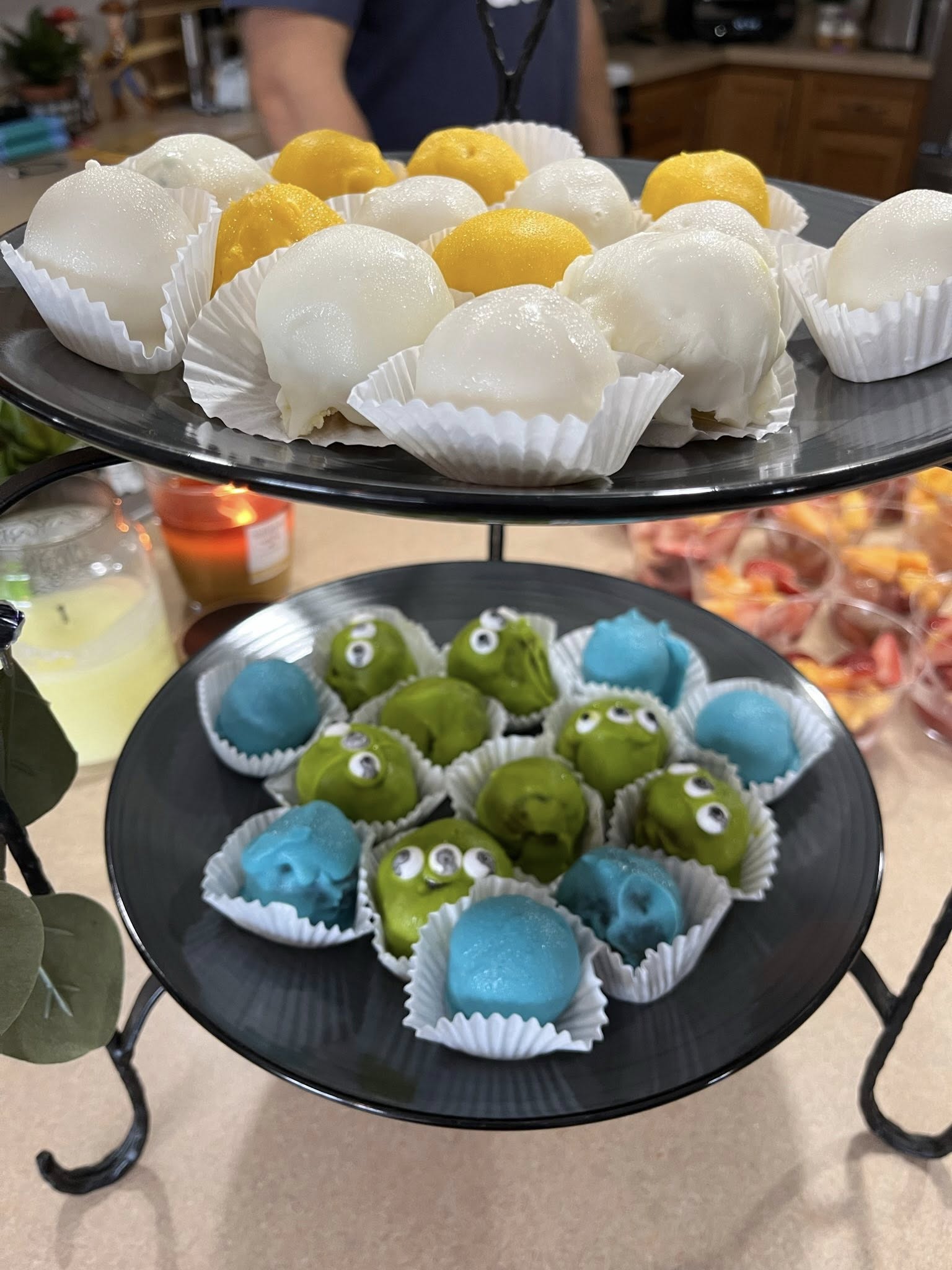 Two-tiered tray serving white and yellow cake pops on the top level and alien-themed green and blue cake pops on the bottom level.