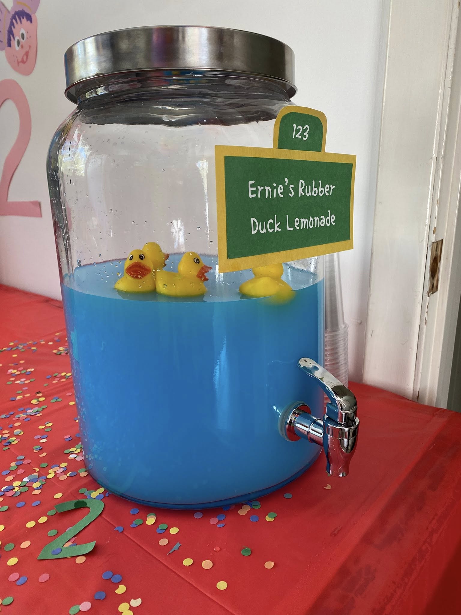 Glass beverage dispenser filled with blue lemonade and floating rubber ducks with a sign labeled Ernie’s Rubber Duck Lemonade