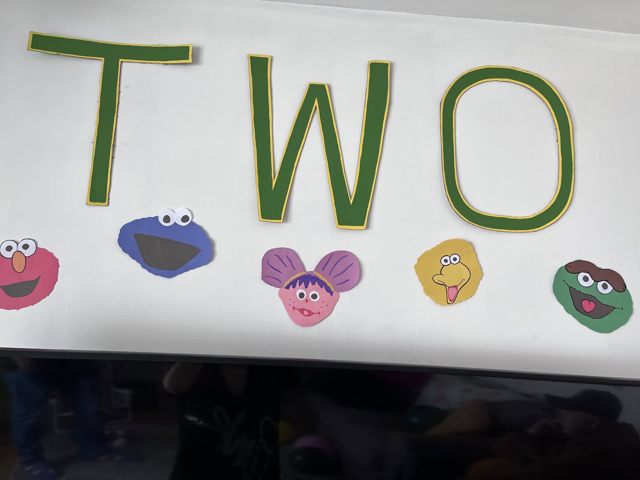 Wall decoration with the word TWO in green letters, themed with Sesame Street character cutouts.