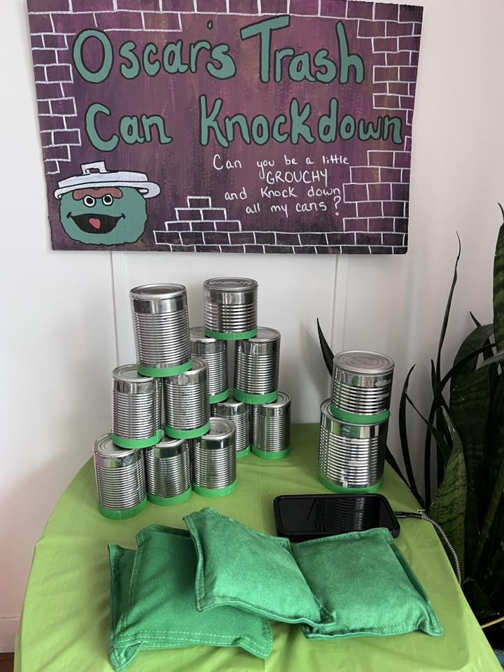 Carnival-style tin can toss game with Oscars Trash Can Knockdown themed signage and green bean bags.